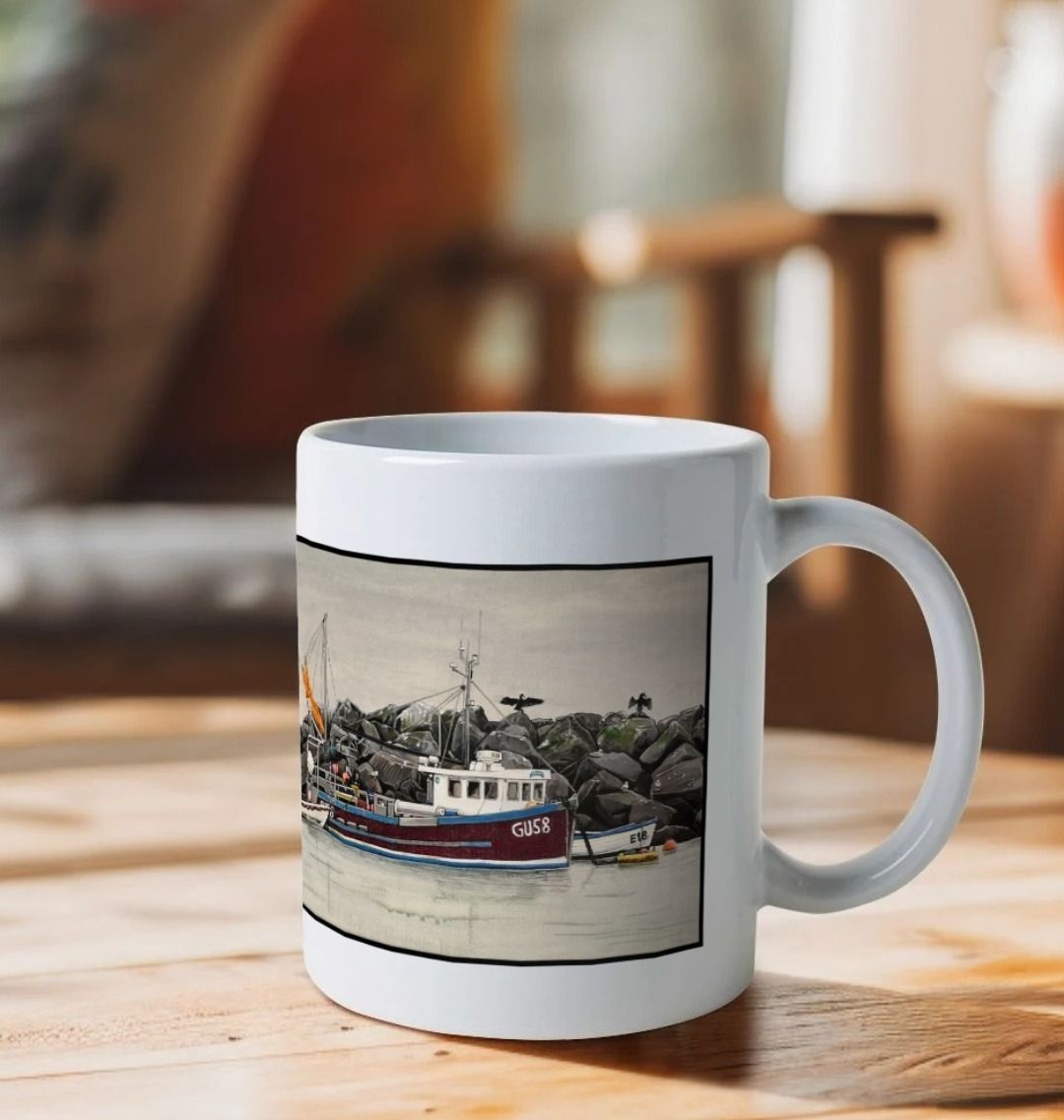 Image of a White Mug on a wooden table featuring 2 details from the painting 'End Of The Line' by Nick Dale. The detail showing the fishing boat is visible. The handle is orientated to the right. The mug depicts a scene where, as the fisherman prepares his catch for unloading at Lyme Regis, the birds line up on the breakwater and patiently await their turn to feed.