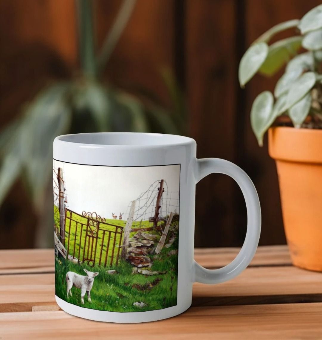 Image of a White Mug on a wooden shelf featuring a copy of the painting 'The Gate' by Nick Dale; as well as a close-up detail of a lamb from the same painting. The handle is orientated to the right. The mug depicts an ornamental garden gate reused by a farmer somewhere in North Devon, probably to the south of Valley of Rocks, Lynton. The animals depicted are all based on animals observed on Lundy Island, Devon.