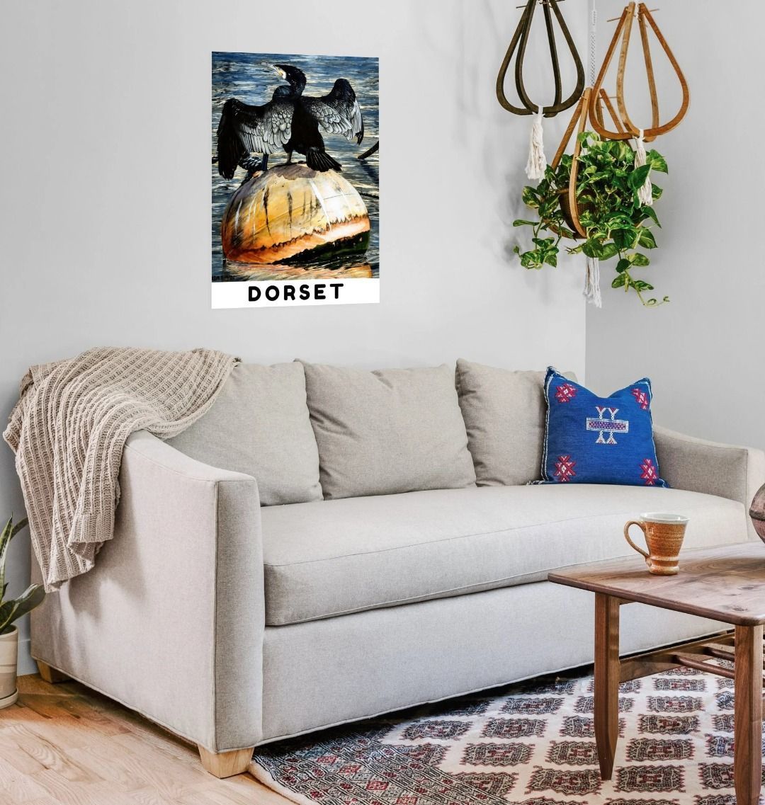 Image of a Large Art Print (A3 size) featuring a copy of the painting 'Cormorant At West Bay' by Nick Dale, with the word 'Dorset' written beneath it. As displayed on a wall above a sofa. The print depicts a close-up of a cormorant sunbathing on a Mooring Buoy in West Bay's harbour in Dorset.