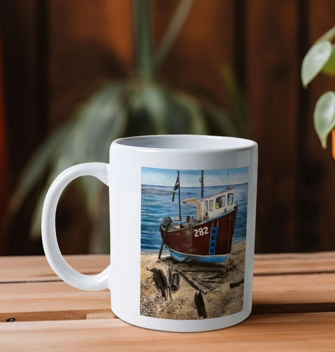 Image of a White Mug on a wooden shelf featuring a copy of the painting 'Relaxing Beer' by Nick Dale. The handle is orientated to the left. The mug depicts a fishing boat beached at Beer, Devon. The wood is laid under the boats to aid in their winching up the shingle beach.