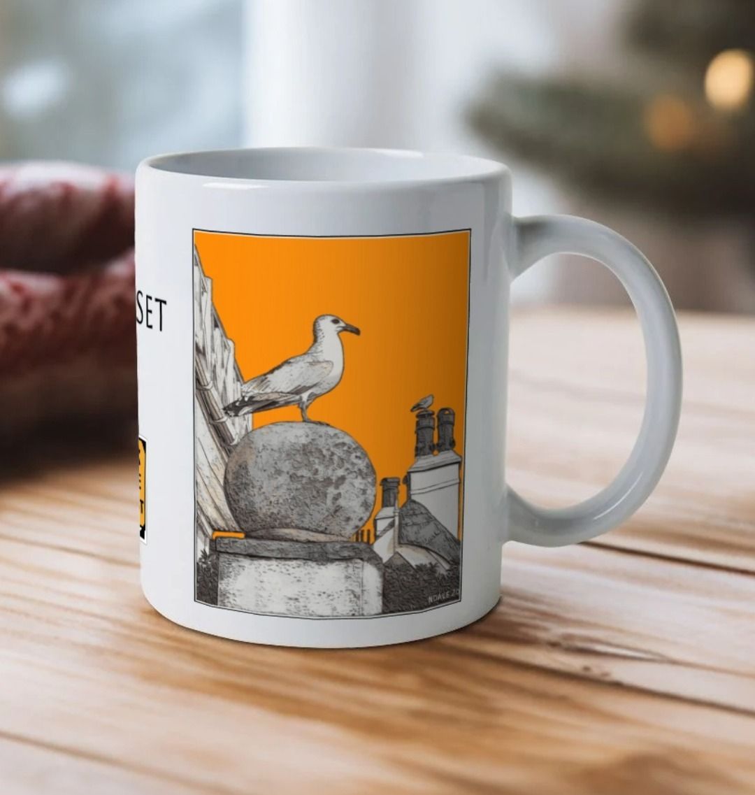 Image of a White Mug on a wooden table featuring a modified copy of the painting 'A View Of The Sea At Lyme Regis' by Nick Dale - this being the 'Orange' version. The handle is orientated to the right.The mug depicts a gull and buildings along Marine Parade, Lyme Regis.