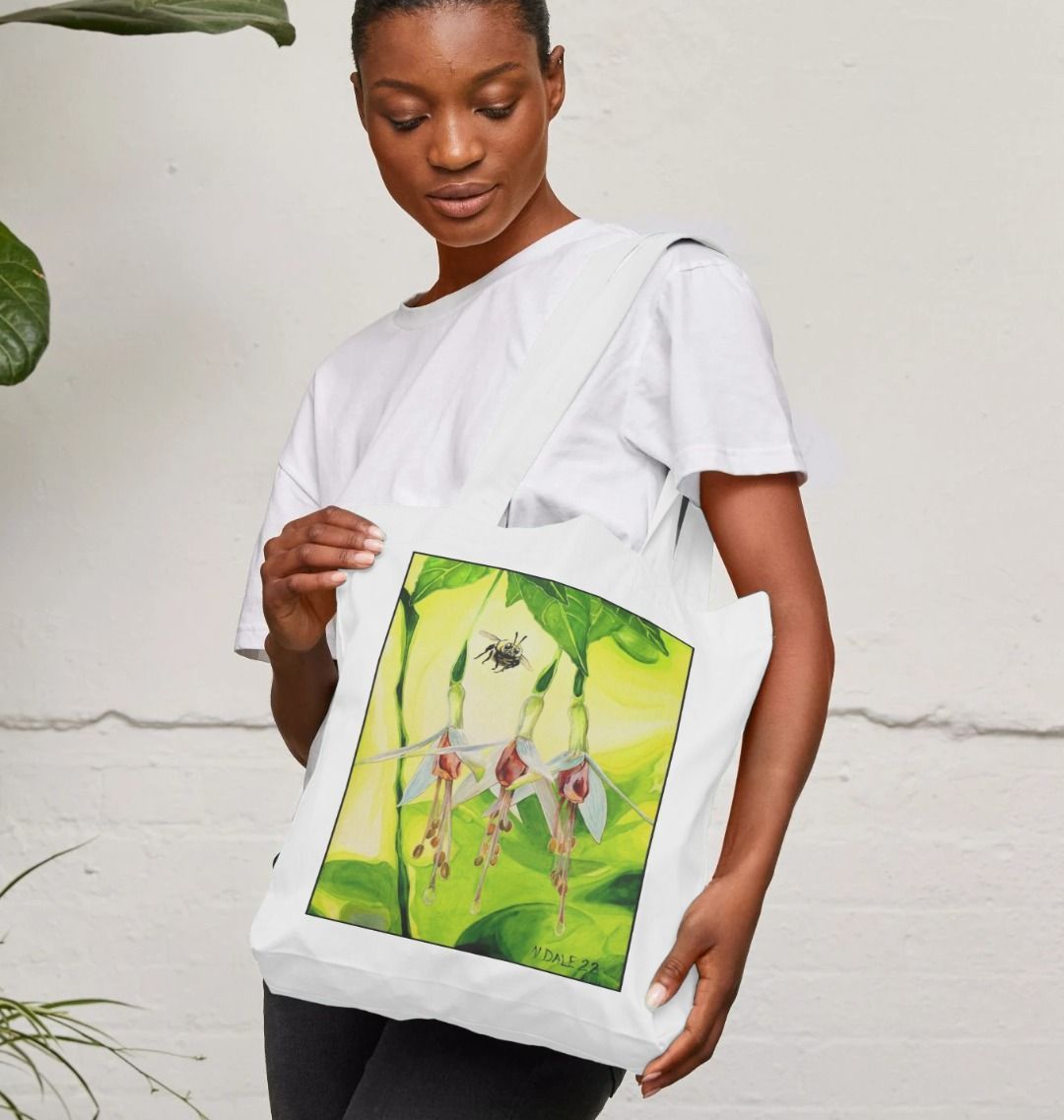 Image of a female model carrying a White Tote Bag featuring a copy of the painting 'The Three Muses' by Nick Dale. The bag depicts a close-up view of a bee approaching its prize. But which will it choose?