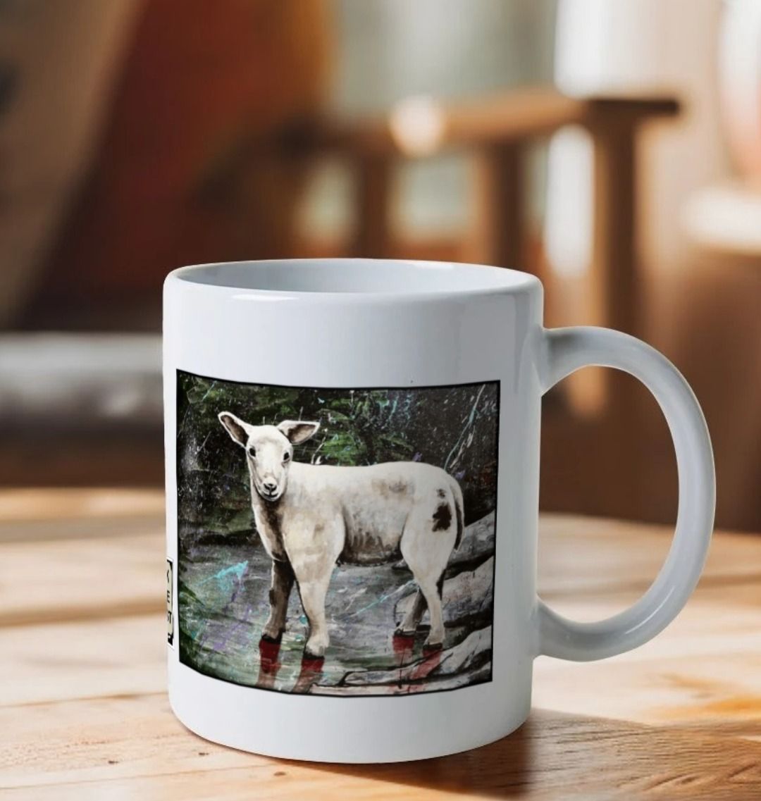 Image of a White Mug on a wooden table featuring a copy of the painting 'The Lamb of Lundy' by Nick Dale. The handle is orientated to the right. The mug depicts a close-up study of a lamb observed on the island of Lundy, Devon.