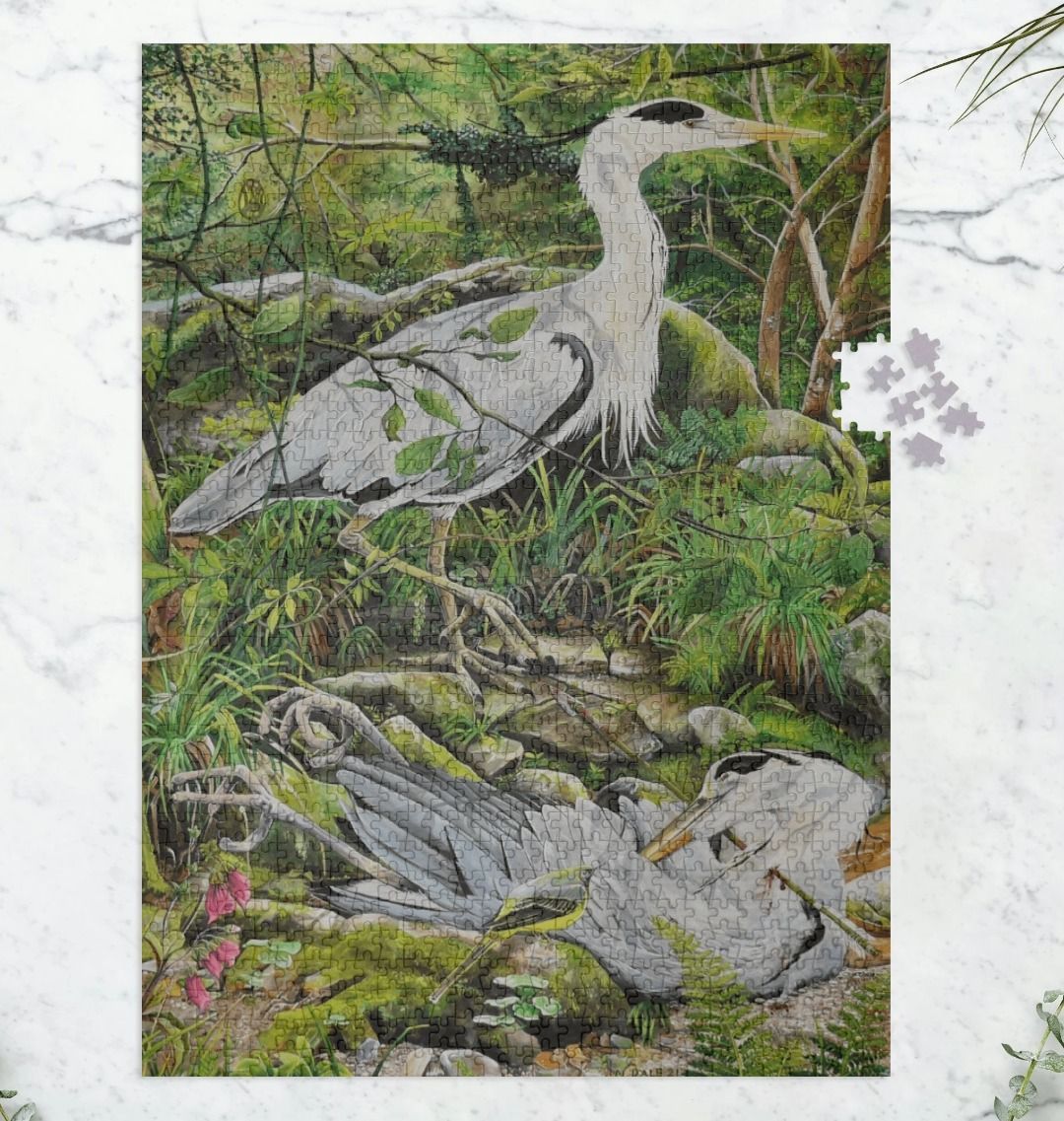 Image of a 1000 Piece Jigsaw Puzzle featuring a copy of the painting 'Fenix Bennu' by Nick Dale. As displayed partially completed on a marble surface. The jigsaw depicts 2 grey herons but is named after the ancient Egyptian god Bennu, which was depicted as a heron and after which the now extinct Bennu Heron is named. The god Bennu may be the origins of the phoenix legend. 'Fenix' is Anglo-Saxon for phoenix and the scene has been transposed to the East Lyn River at Lynmouth in Devon.