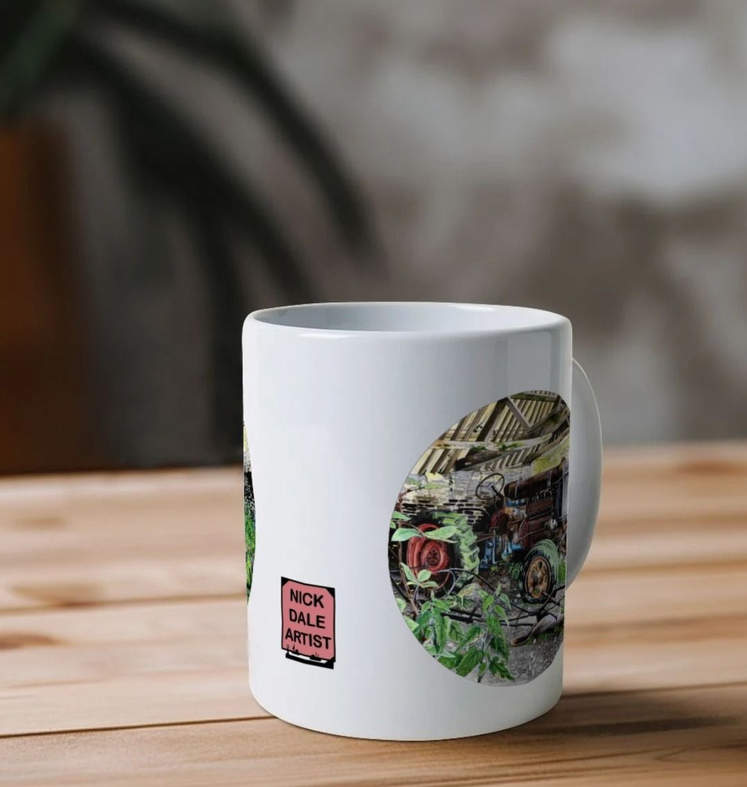 Image of a White Mug on a table featuring a copy of the painting 'A Well Deserved Rest At Tyneham' by Nick Dale. Image also shows the artist's logo on the mug. The mug handle is obscured behind the mug. The mug depicts a Fordson Major tractor laid up in a farm building at the abandoned village of Tyneham in Dorset.