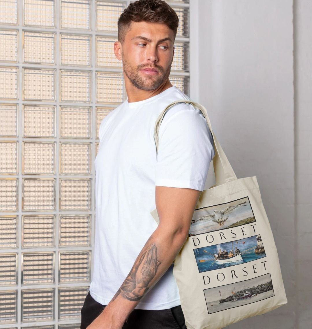 Image of male model holding Natural Tote Bag featuring 3 Scenes Of Dorset. The scenes are derived from 3 original paintings by Nick Dale  and are separated from each other vertically by the word 'Dorset'. 