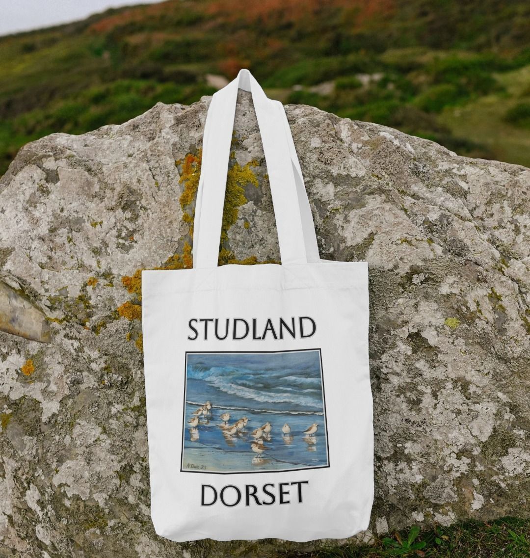 Image of White Tote Bag featuring a copy of the painting 'Studland Misty Morning' by Nick Dale. Shown lying on a rock. The bag depicts Dunlins on Studland Beach (Dorset) on a crisp and misty morning.