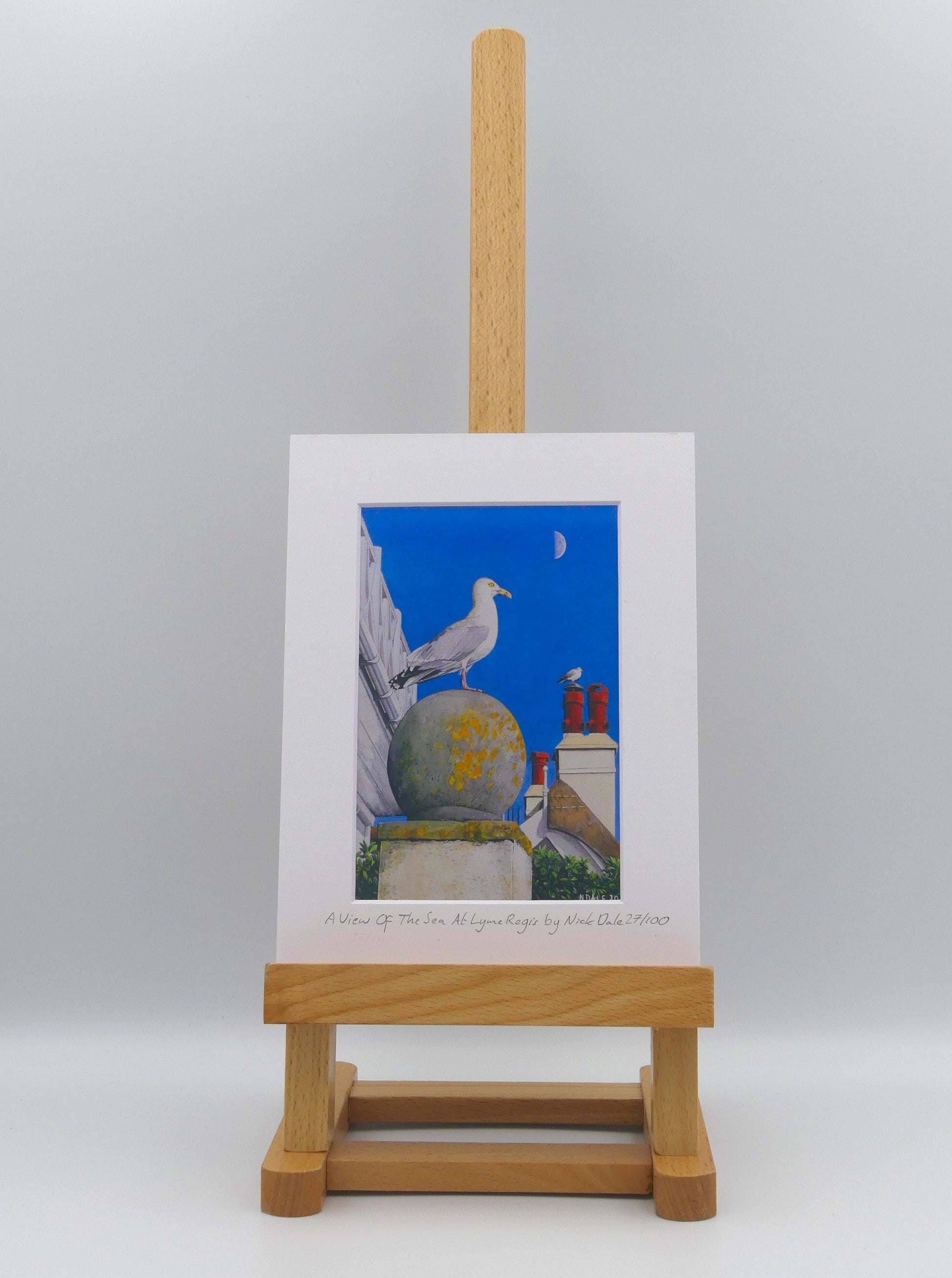 Image of Small Art Print featuring a copy of the painting 'A View Of The Sea At Lyme Regis' by Nick Dale. The print depicts a gull and buildings along Marine Parade, Lyme Regis. The print is situated on a small easel.