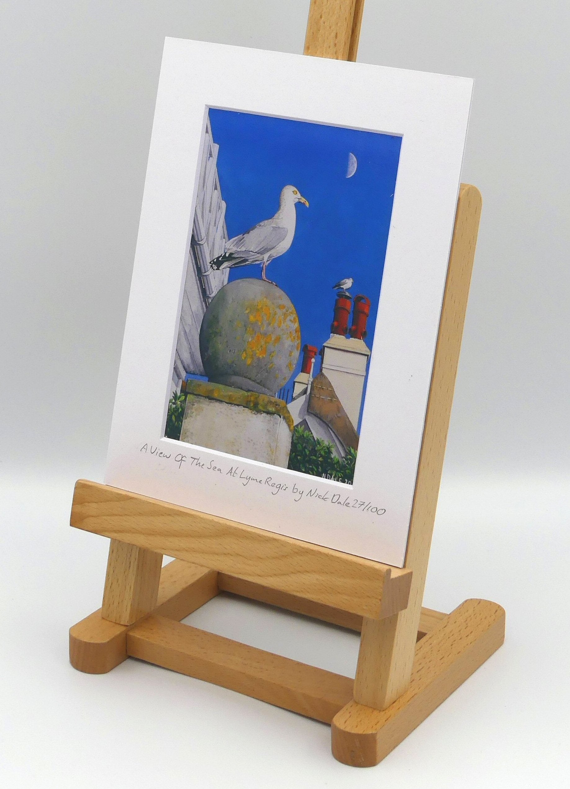 Image of Small Art Print featuring a copy of the painting 'A View Of The Sea At Lyme Regis' by Nick Dale. The print depicts a gull and buildings along Marine Parade, Lyme Regis. The print is situated on a small easel.