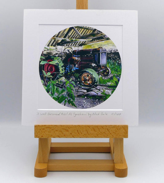Image of Square Medium Art Print featuring a copy of the painting 'A Well Deserved Rest At Tyneham' by Nick Dale. The print depicts a Fordson Major tractor laid up in a farm building at the abandoned village of Tyneham in Dorset. The print is situated on a small easel.