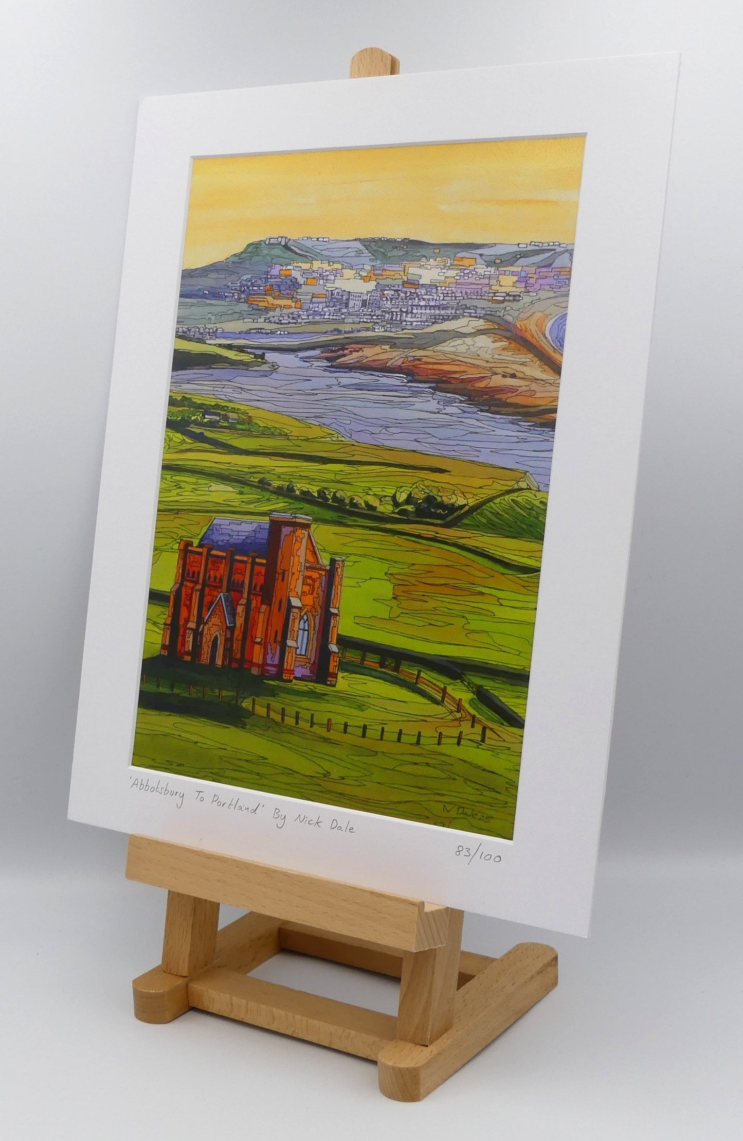 Image of a Medium Art Print featuring a copy of the painting 'Abbotsbury To Portland' by Nick Dale. The print depicts the view along the Dorset coast from St Catherine's Chapel above Abbotsbury, across The Fleet lagoon to Chesil Beach and ultimately to Portland beyond it. The print is situated on a small easel.