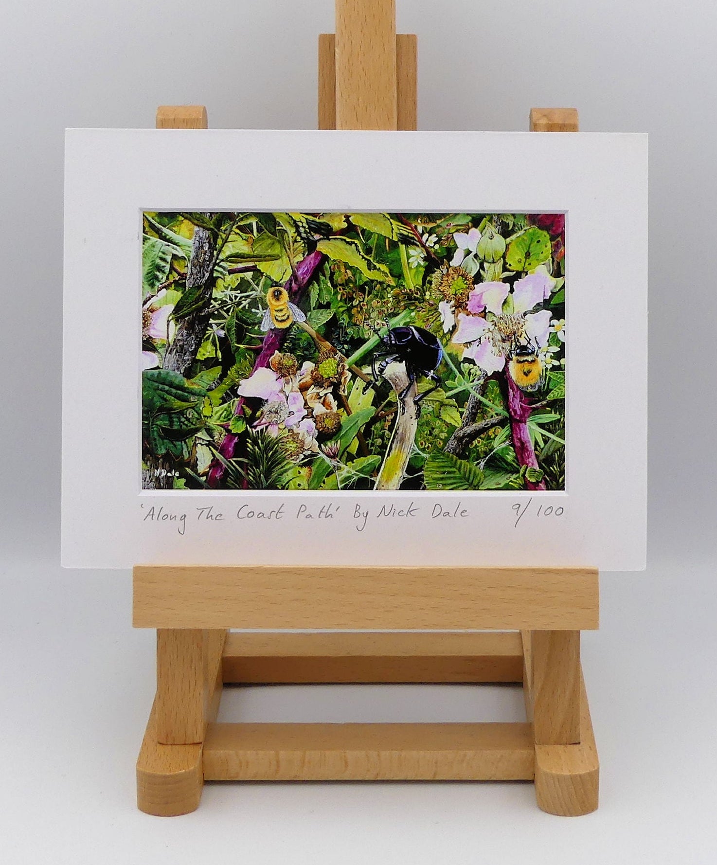 Image of a Small Art Print featuring a copy of the painting 'Along The Coast Path' by Nick Dale. The print depicts a close-up view of a coast path hedgerow on the Dorset/Devon border. A bloody-nosed beetle edges its way along a plant stem whilst bees attend the bramble flowers. The print is situated on a small easel.