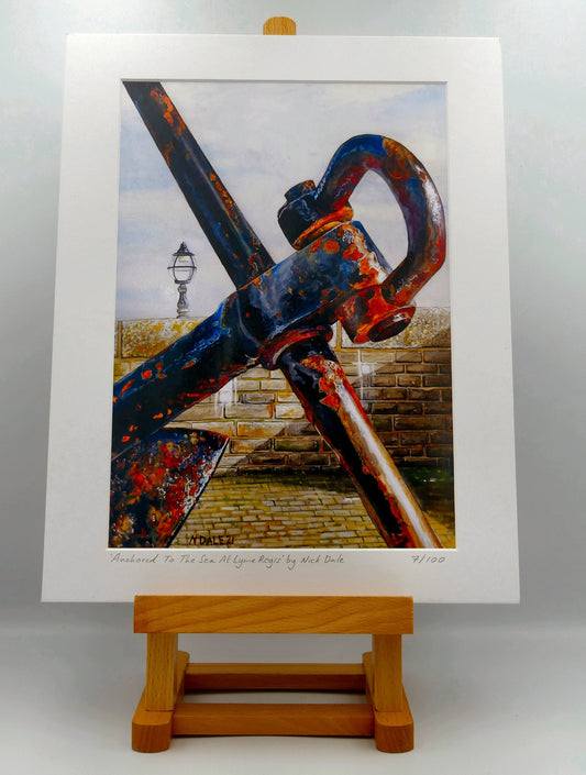 Image of Medium Art Print featuring a copy of the painting 'Anchored To The Sea At Lyme Regis' by Nick Dale. The print depicts a close up of a large anchor situated on Lyme Regis seafront along Gun Cliff Walk. The anchor was gifted from Portland Royal Naval Base in memory of all the Lyme Regis men and women who made their living from the sea. The print is situated on a small easel.