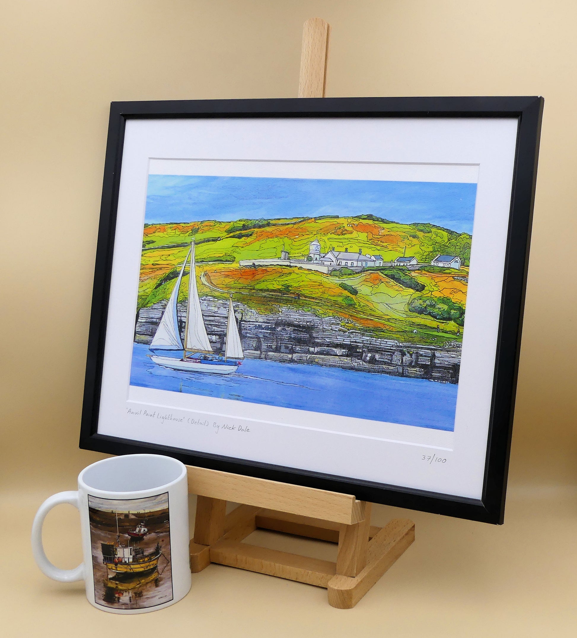 Image of a Medium Art Print featuring a copy of the painting 'Anvil Point Lighthouse' by Nick Dale. The print depicts the part of the original painting showing the Anvil Point Lighthouse at Durlston Country Park, Swanage. Based on the view from the paddle-steamer Waverley. The print is situated on a small easel in a black frame next to a mug.