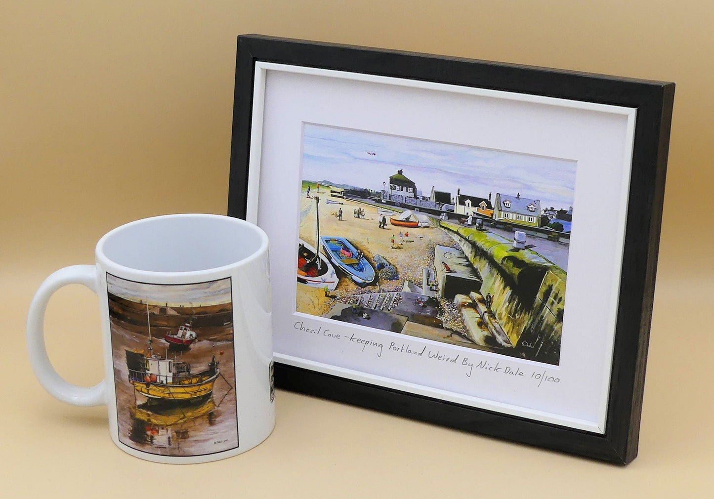 Image of a Small Art Print featuring a copy of the painting 'Chesil Cove - Keeping Portland Weird' by Nick Dale. The print depicts the end of Chesil Beach where it meets Portland at Chesil Cove. In the scene the size of the people is not affected by their distance from the foreground, hence making their appearance slightly surreal. The print is situated in a black frame next to a mug.