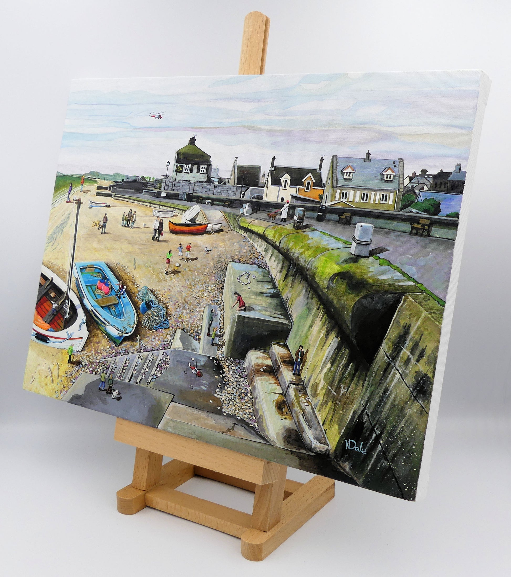 Image of the original painting 'Chesil Cove - Keeping Portland Weird' by Nick Dale on a small easel.  The scene depicts the end of Chesil Beach where it meets Portland at Chesil Cove. In the painting the size of the people is not affected by their distance from the foreground, hence making their appearance slightly surreal. 
