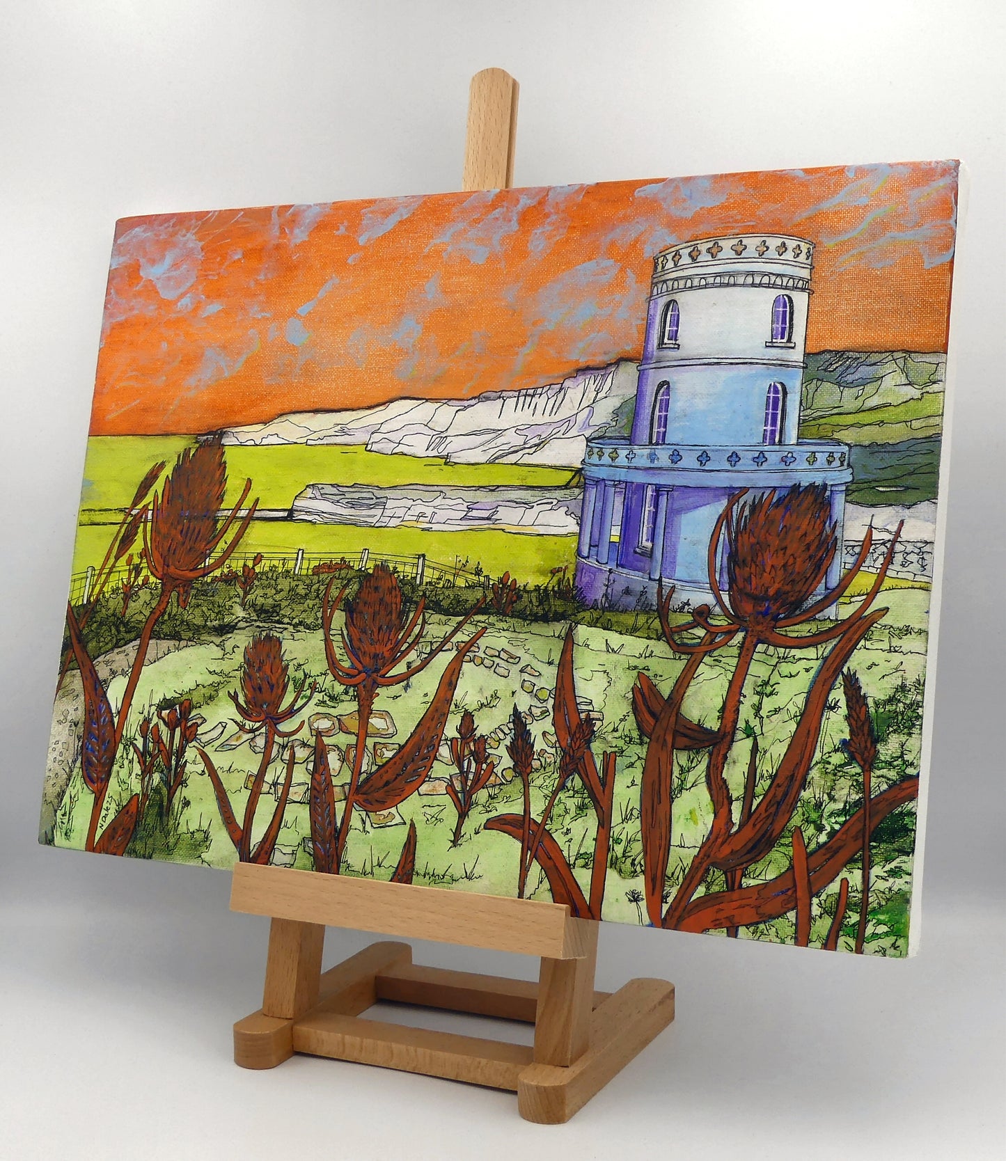 Image of the original painting 'Clavell Tower, Kimmeridge Bay' by Nick Dale on an easel. The painting depicts Clavell Tower (which is also known as the Clavell Folly or the Kimmeridge Tower) situated on the cliffs overlooking Kimmeridge Bay on the Isle of Purbeck, Dorset. 
The tower; which was built in 1830, is seen in its current position with the original footings visible in the foreground after the tower was moved further back from the cliff edge in 2006. 