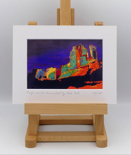 Image of a Small Art Print featuring a copy of the painting 'Corfe Castle Illuminated' by Nick Dale. The print depicts a view of the ruins of Corfe Castle at night from within the outer bailey; with the south-west gatehouse on the left and the keep on top of the central hilltop on the right.  The print is situated on a small easel.