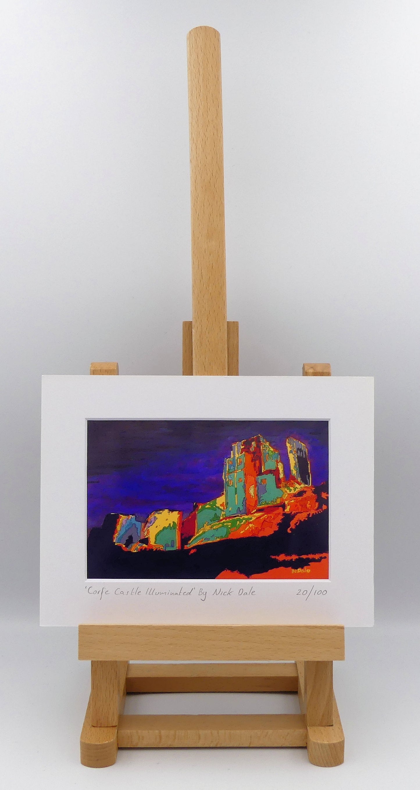 Image of a Small Art Print featuring a copy of the painting 'Corfe Castle Illuminated' by Nick Dale. The print depicts a view of the ruins of Corfe Castle at night from within the outer bailey; with the south-west gatehouse on the left and the keep on top of the central hilltop on the right. The print is situated on a small easel.