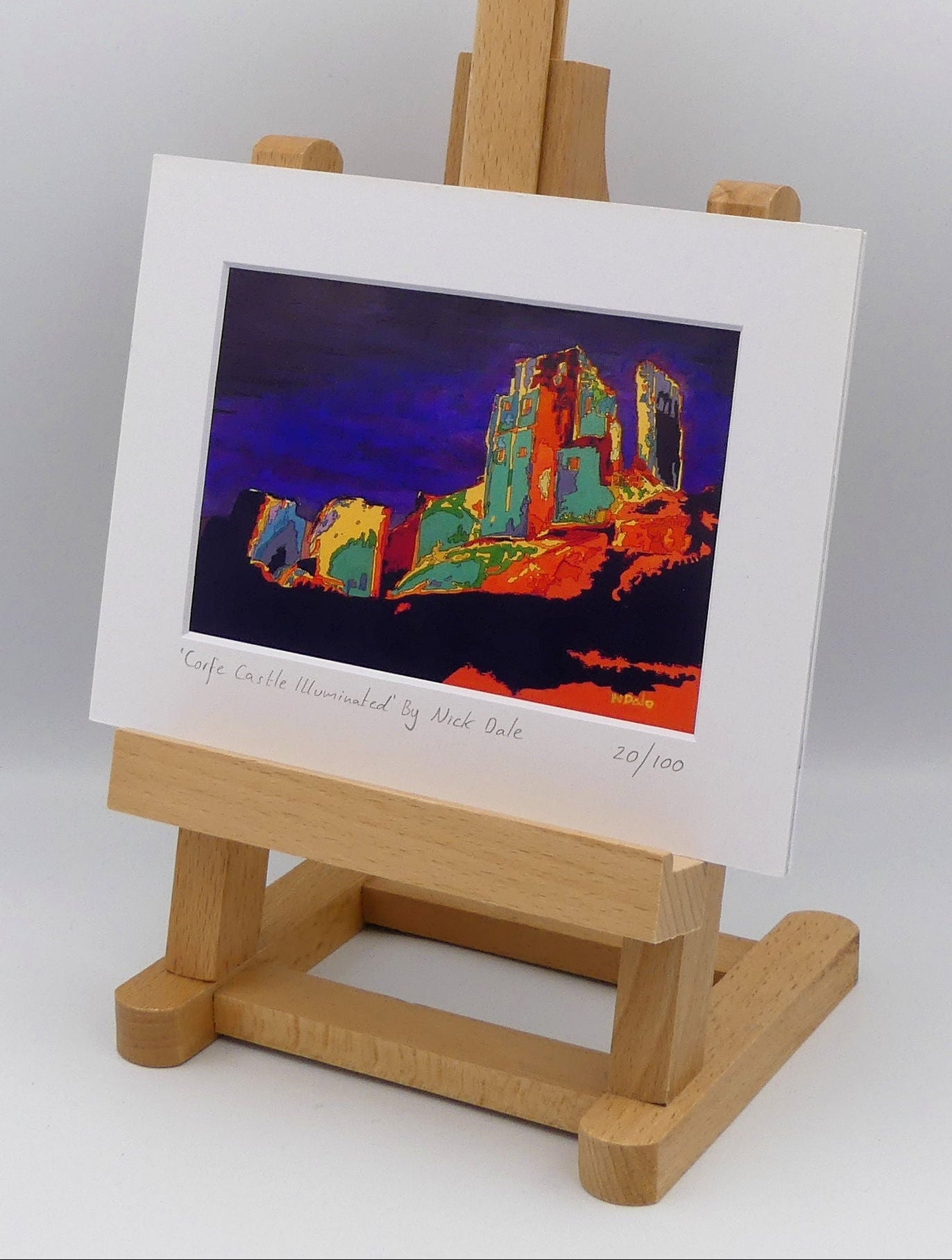Image of a Small Art Print featuring a copy of the painting 'Corfe Castle Illuminated' by Nick Dale. The print depicts a view of the ruins of Corfe Castle at night from within the outer bailey; with the south-west gatehouse on the left and the keep on top of the central hilltop on the right. The print is situated on a small easel.