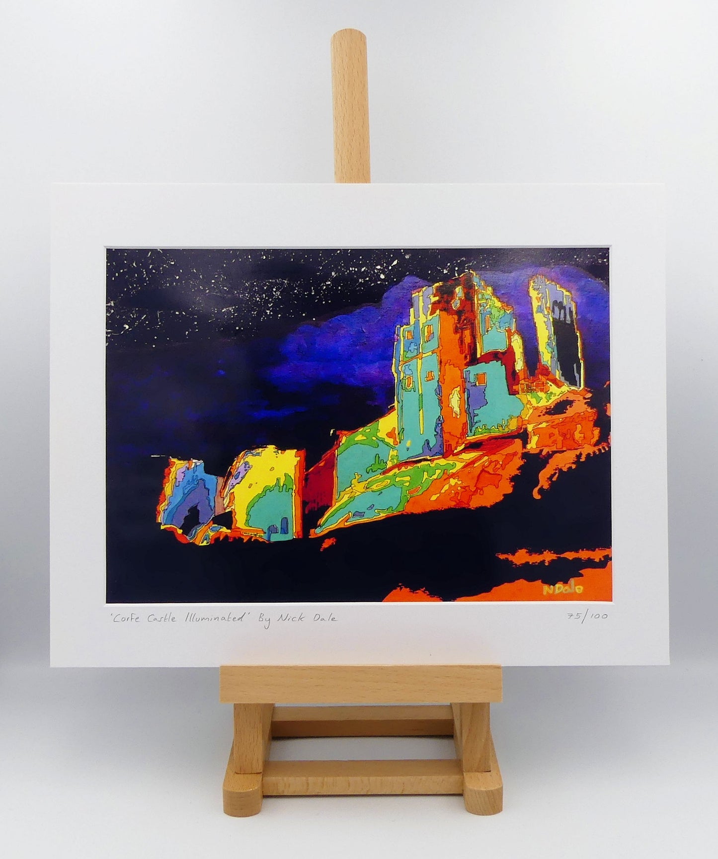 Image of a Medium Art Print featuring a copy of the painting 'Corfe Castle Illuminated' by Nick Dale. The print depicts a view of the ruins of Corfe Castle at night from within the outer bailey; with the south-west gatehouse on the left and the keep on top of the central hilltop on the right. The print is situated on a small easel.