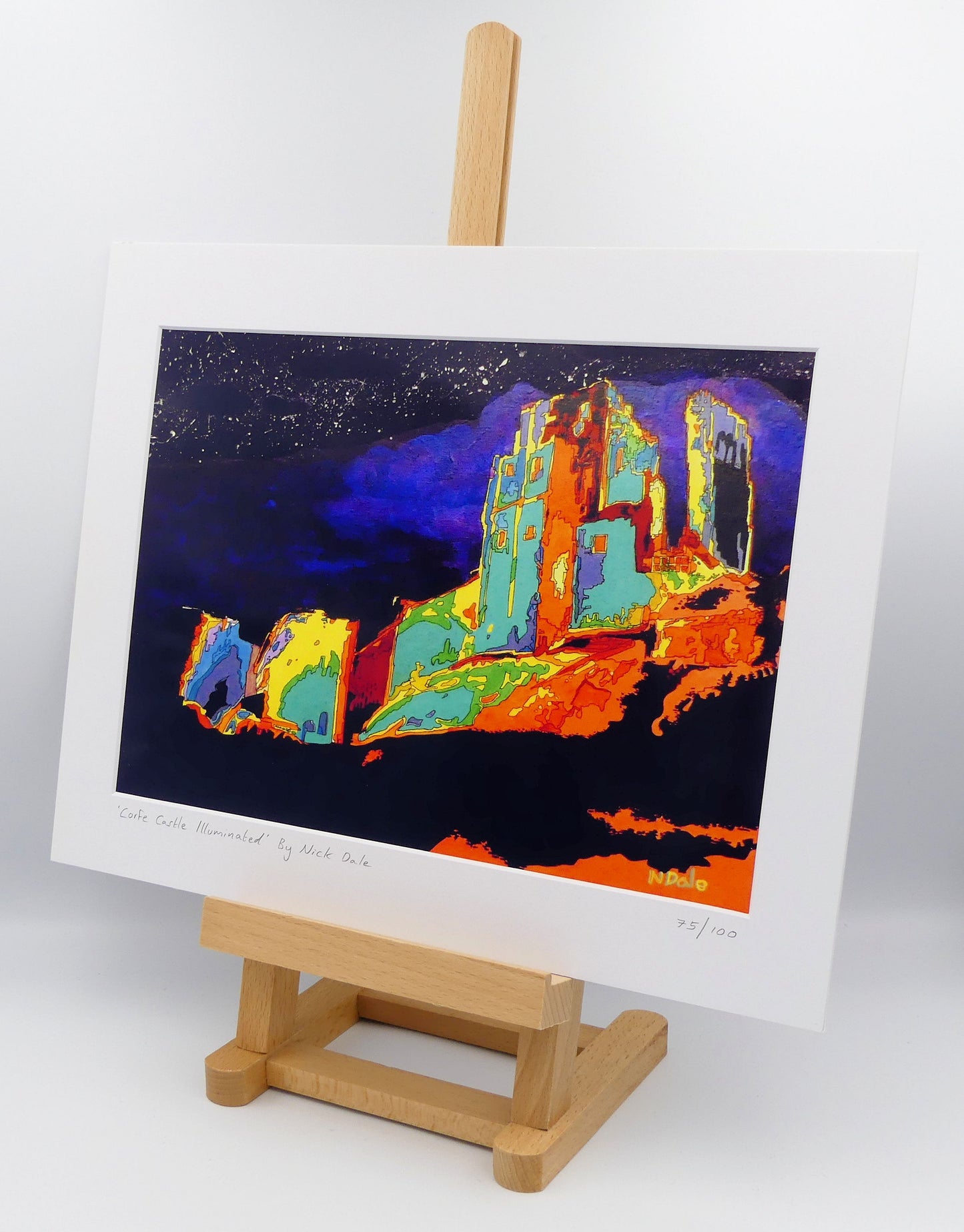 Image of a Medium Art Print featuring a copy of the painting 'Corfe Castle Illuminated' by Nick Dale. The print depicts a view of the ruins of Corfe Castle at night from within the outer bailey; with the south-west gatehouse on the left and the keep on top of the central hilltop on the right. The print is situated on a small easel.