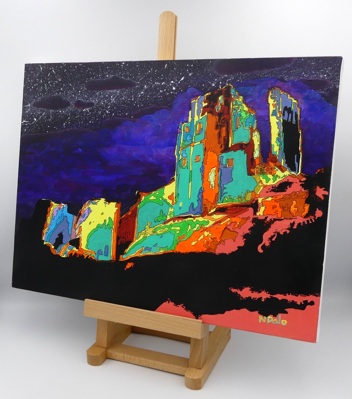 Image of the original painting 'Corfe Castle Illuminated' by Nick Dale on a small easel. The painting depicts a view of the ruins of Corfe Castle at night from within the outer bailey; with the south-west gatehouse on the left and the keep on top of the central hilltop on the right.