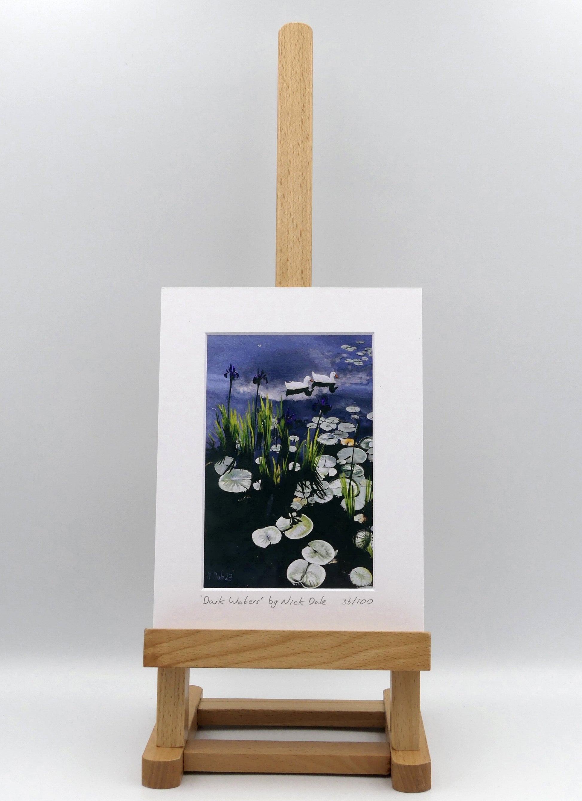 Image of a Small Art Print featuring a copy of the painting 'Dark Waters' by Nick Dale. The print depicts lily pads, irises and ducks on a pond at Knightshayes Court, Devon. The print is situated on a small easel.