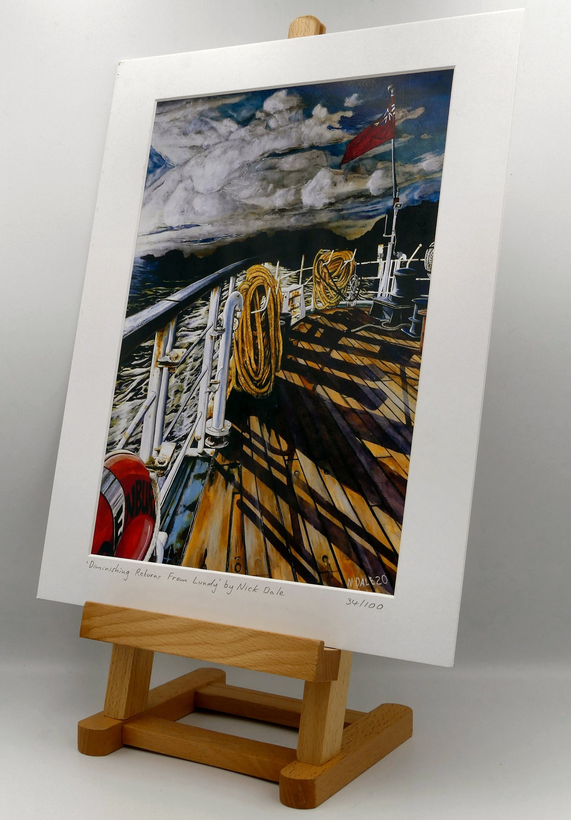 Image of Medium Art Print featuring a copy of the painting 'Diminishing Returns From Lundy' by Nick Dale. The print depicts the stern of the ship MS Oldenburg as it returns to the mainland from Lundy Island, Devon. As the sun goes down it casts long shadows on the deck. whilst the flag flutters in the breeze. The Silhouette of the island can be seen diminishing into the background. The print is situated on a small easel.