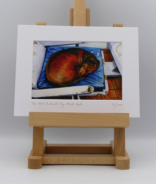 Image of a Small Art Print featuring a copy of the painting 'Do Not Disturb' by Nick Dale. The print depicts a miniature dachshund dog curled up on a favourite seat. Its gaze clearly indicates that it is not keen on being evicted from its current location and slumbering state. The print is situated on a small easel.