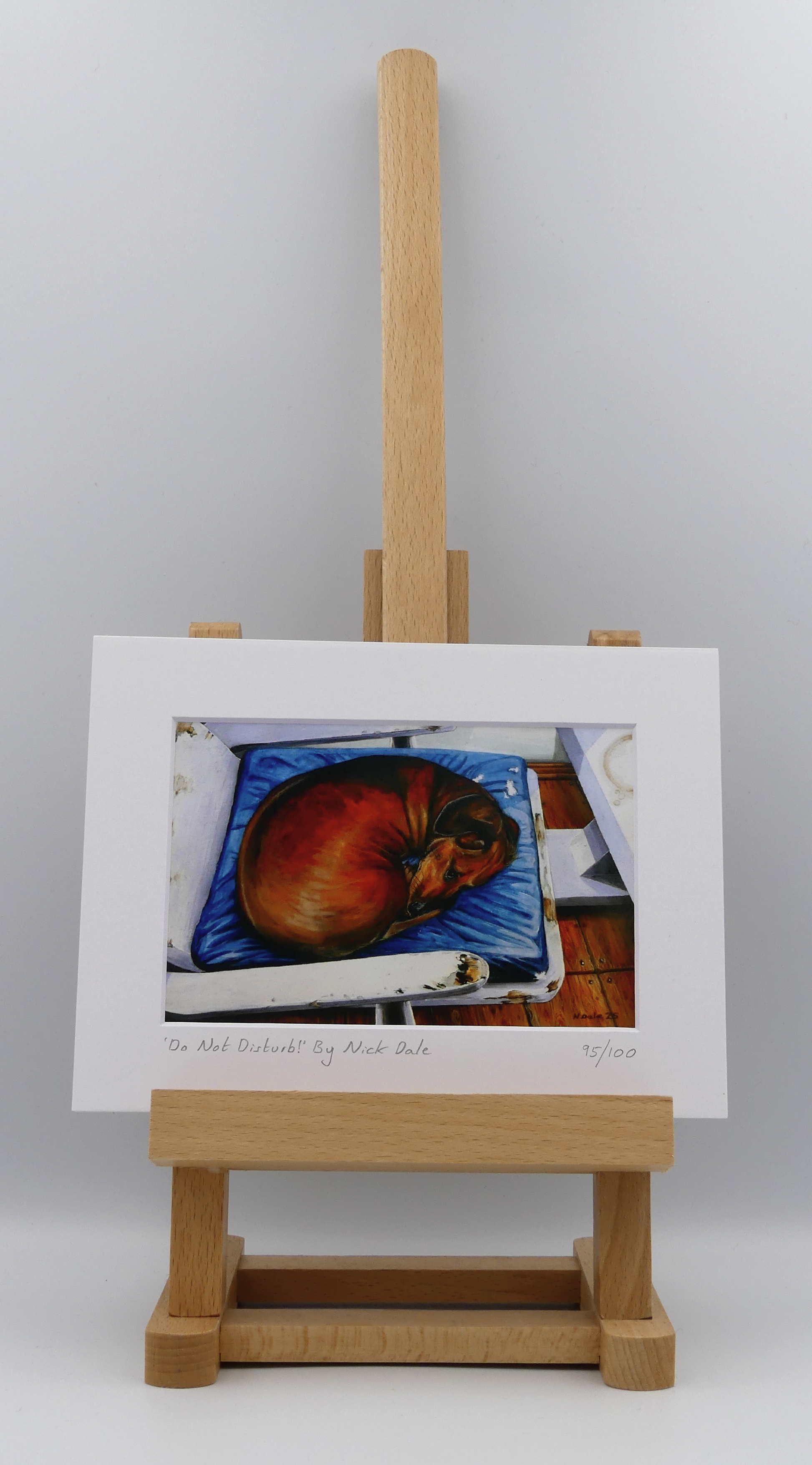 Image of a Small Art Print featuring a copy of the painting 'Do Not Disturb' by Nick Dale. The print depicts a miniature dachshund dog curled up on a favourite seat. Its gaze clearly indicates that it is not keen on being evicted from its current location and slumbering state. The print is situated on a small easel.