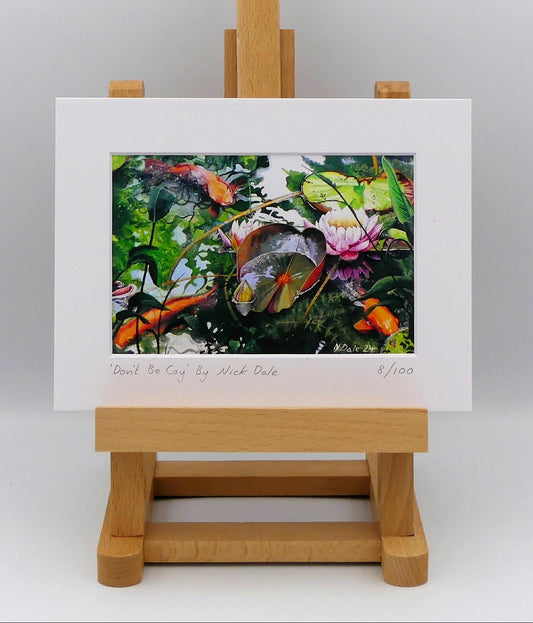 Image of a Small Art Print featuring a copy of the painting 'Don't Be Coy' by Nick Dale. The print depicts 3 koi carp along with water lilies and their flowers. The painting is based on fish and lilies observed at Bennetts Water Gardens in Weymouth, Dorset. The title is a play on the homophones 'Coy' and 'Koi'.  The print is situated on a small easel.