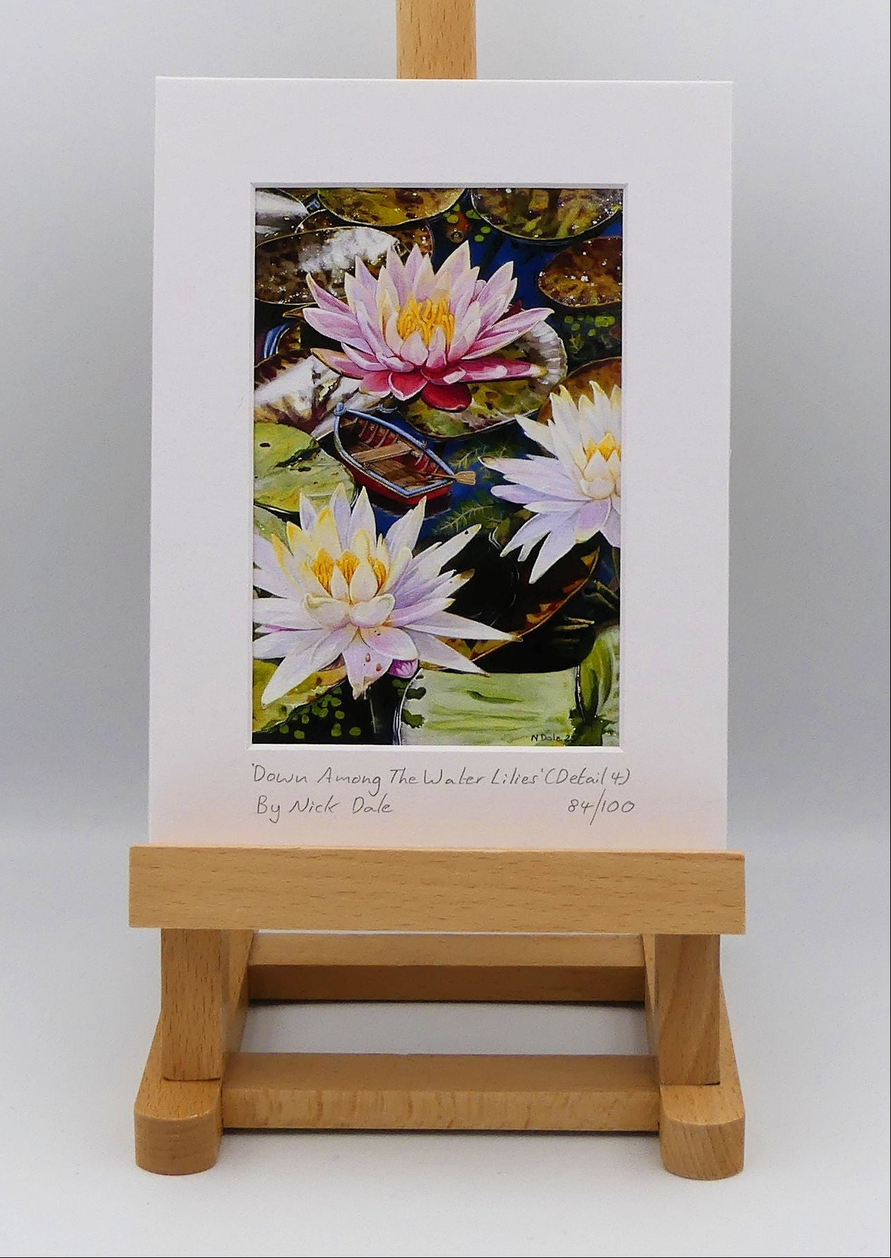 Image of a Small Art Print featuring a copy of a detail from the painting 'Down Among The Water Lilies' by Nick Dale. The print depicts the part of the original painting showing the rowing boat and a close-up view of the water lilies at Bennetts Water Gardens in Weymouth, with the twist of the boat being shrunk down to lilliputian dimensions.  The print is situated on a small easel.