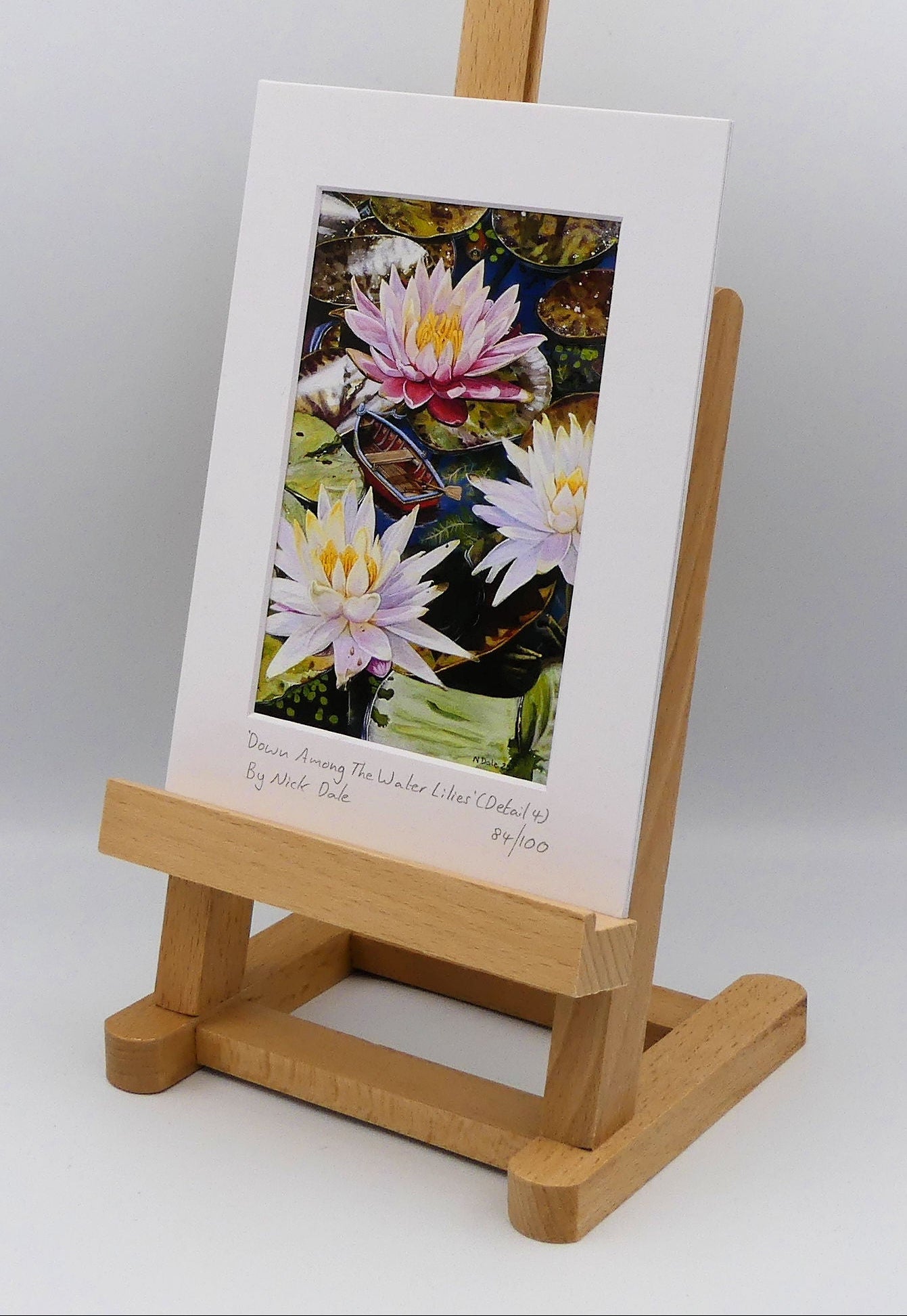 Image of a Small Art Print featuring a copy of a detail from the painting 'Down Among The Water Lilies' by Nick Dale. The print depicts the part of the original painting showing the rowing boat and a close-up view of the water lilies at Bennetts Water Gardens in Weymouth, with the twist of the boat being shrunk down to lilliputian dimensions. The print is situated on a small easel.
