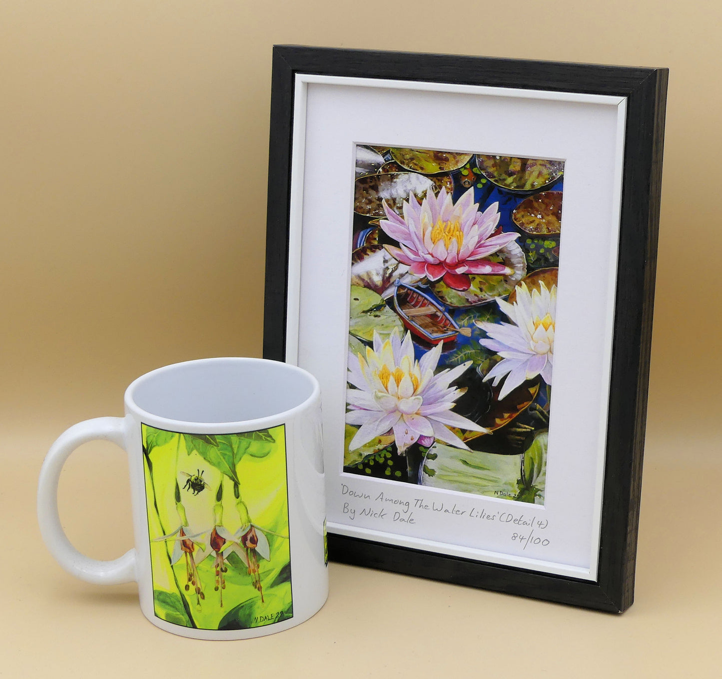 Image of a Small Art Print featuring a copy of a detail from the painting 'Down Among The Water Lilies' by Nick Dale. The print depicts the part of the original painting showing the rowing boat and a close-up view of the water lilies at Bennetts Water Gardens in Weymouth, with the twist of the boat being shrunk down to lilliputian dimensions. The print is situated in a black frame next to a mug.