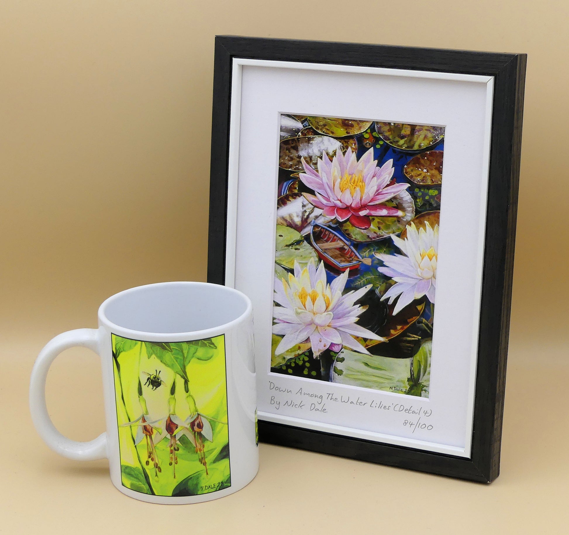 Image of a Small Art Print featuring a copy of a detail from the painting 'Down Among The Water Lilies' by Nick Dale. The print depicts the part of the original painting showing the rowing boat and a close-up view of the water lilies at Bennetts Water Gardens in Weymouth, with the twist of the boat being shrunk down to lilliputian dimensions. The print is situated in a black frame next to a mug.