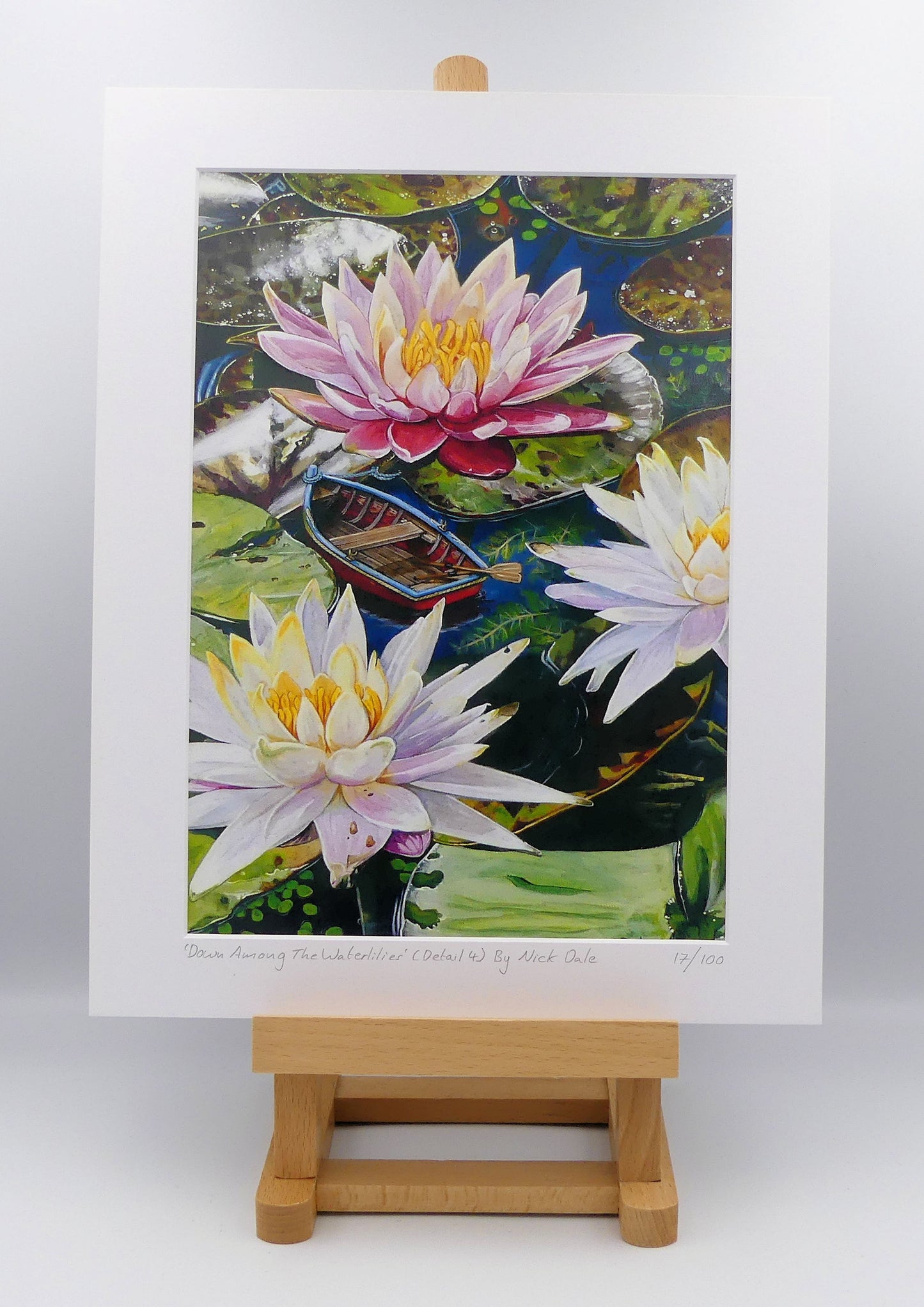 Image of a Medium Art Print featuring a copy of a detail from the painting 'Down Among The Water Lilies' by Nick Dale. The print depicts the part of the original painting showing the rowing boat and a close-up view of the water lilies at Bennetts Water Gardens in Weymouth, with the twist of the boat being shrunk down to lilliputian dimensions. The print is situated on a small easel.