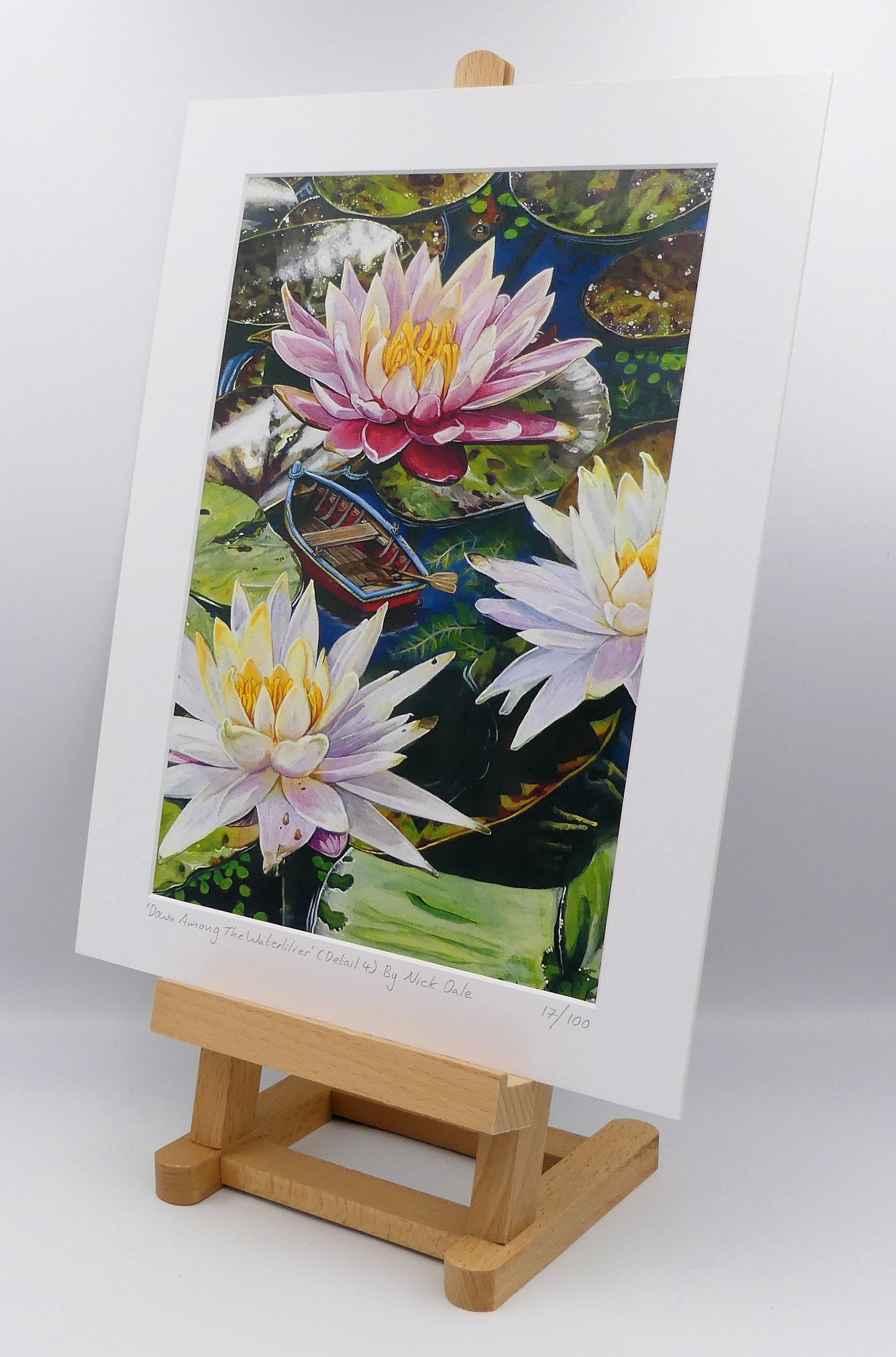 Image of a Medium Art Print featuring a copy of a detail from the painting 'Down Among The Water Lilies' by Nick Dale. The print depicts the part of the original painting showing the rowing boat and a close-up view of the water lilies at Bennetts Water Gardens in Weymouth, with the twist of the boat being shrunk down to lilliputian dimensions. The print is situated on a small easel.