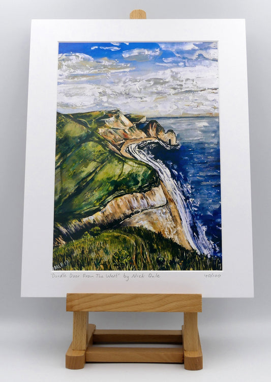 Image of a Medium Art Print featuring a copy of the painting 'Durdle Door From The West:' by Nick Dale. The print depicts a view along the Jurassic Coast to the famous Dorset limestone arch landmark, as seen from the coastal path to the west. The print is situated on a small easel.