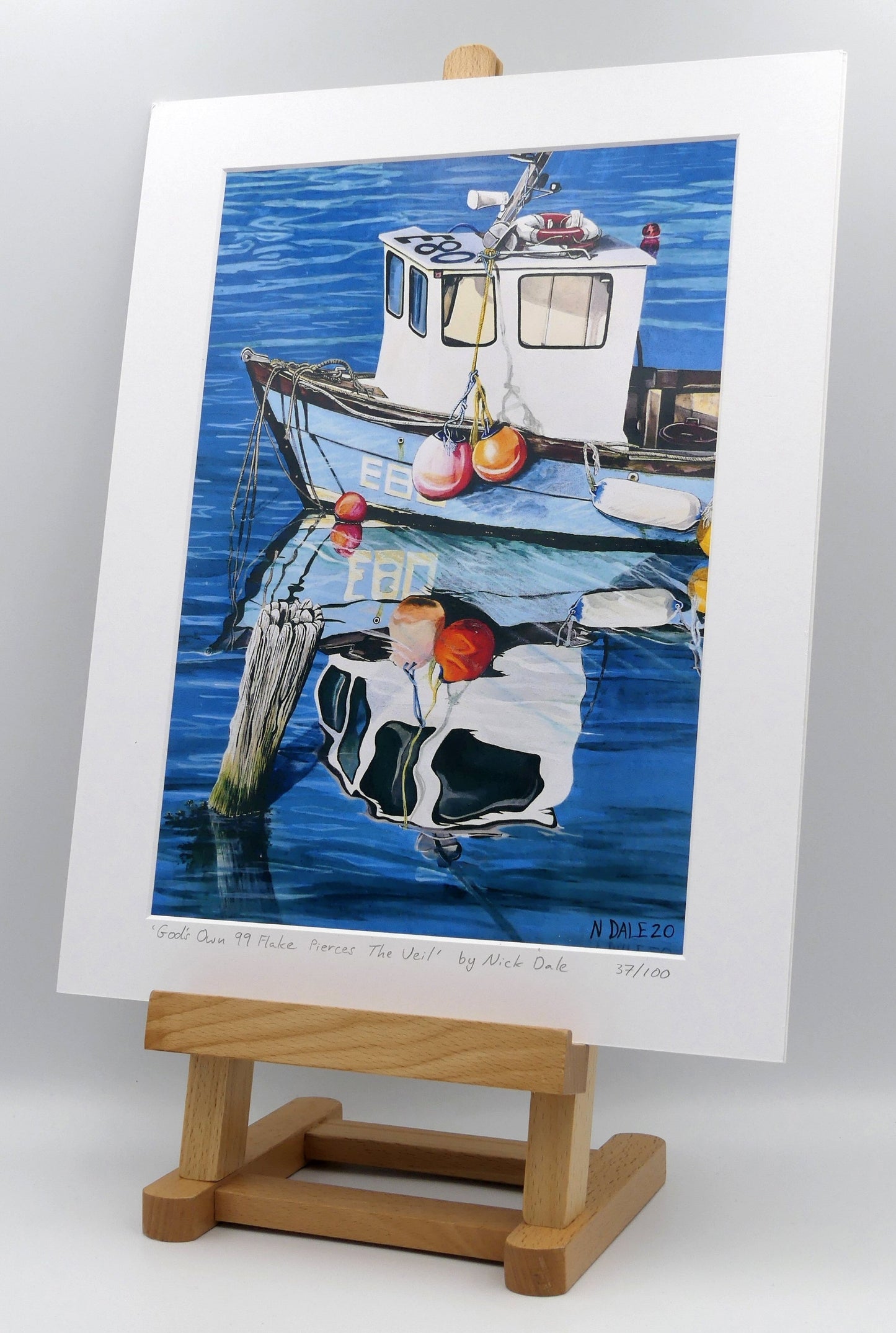 Image of a Medium Art Print featuring a copy of the painting 'God's Own 99 Flake Pierces The Veil' by Nick Dale. The print depicts a fishing boat at rest within the harbour of Lyme Regis, Dorset. The title is based on the similarity of the wooden pile to a chocolate flake as inserted into an ice cream cone. This seemed appropriate given the draw of the town to tourists. The print is situated on a small easel.