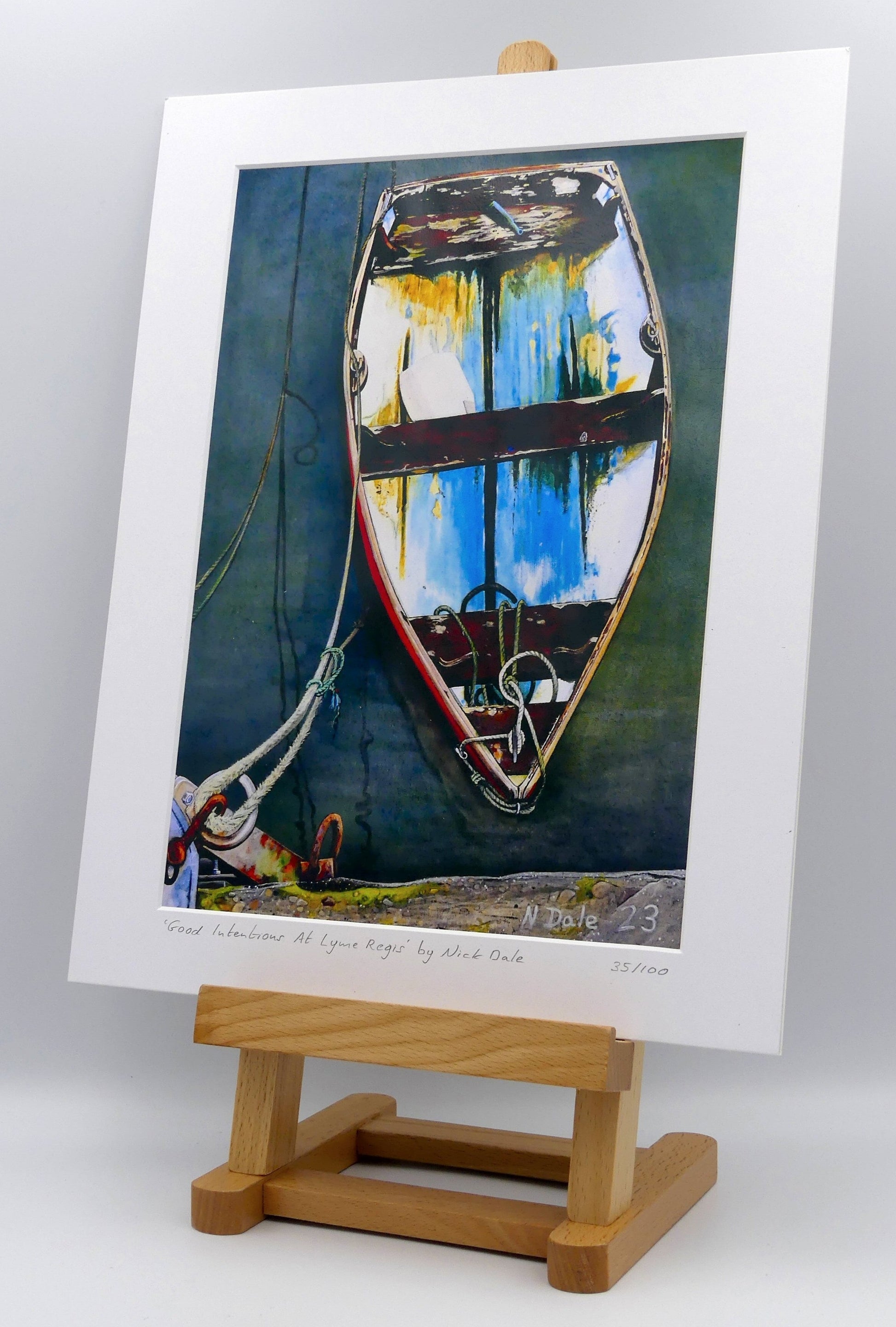 Image of a Medium Art Print featuring a copy of the painting 'Good Intentions at Lyme Regis' by Nick Dale. The print depicts a small wooden rowing boat tied up in Lyme Regis harbour, Dorset. The print is situated on a small easel.