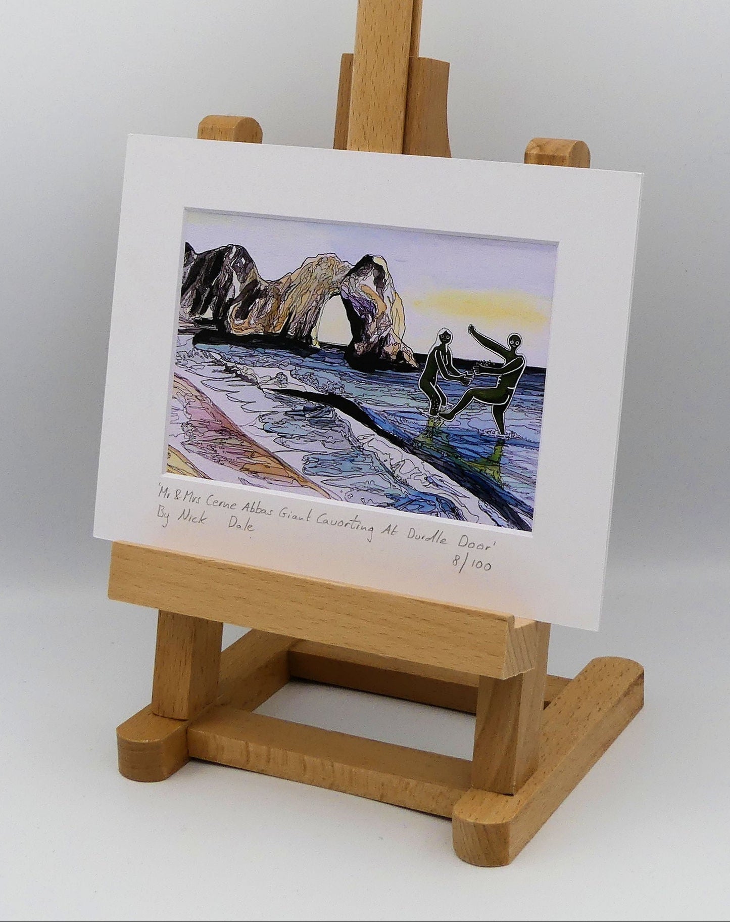 Image of a Small Art Print featuring a copy of the painting 'Mr & Mrs Cerne Abbas Giant Cavorting At Durdle Door' by Nick Dale. The scene imagines the future Mr & Mrs Cerne Abbas Giant's first date at Durdle Door; where they cavort in the water in front of the famous Dorset landmark. The print is situated on a small easel.