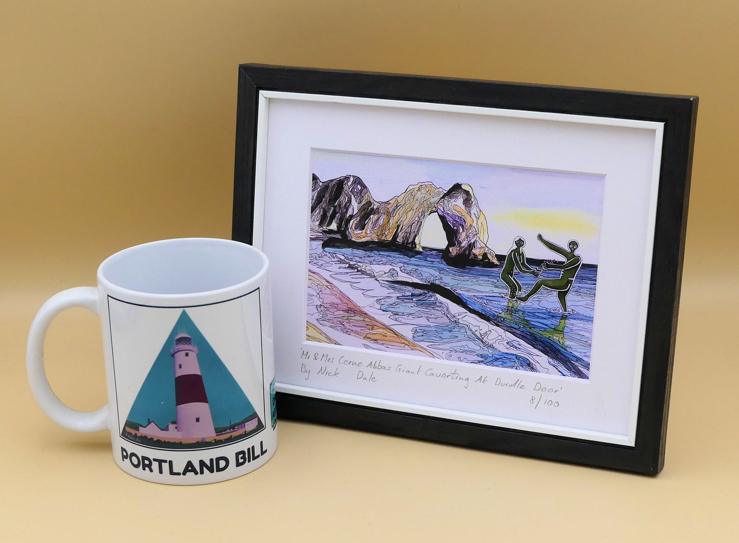 Image of a Small Art Print featuring a copy of the painting 'Mr & Mrs Cerne Abbas Giant Cavorting At Durdle Door' by Nick Dale. The scene imagines the future Mr & Mrs Cerne Abbas Giant's first date at Durdle Door; where they cavort in the water in front of the famous Dorset landmark. The print is situated in a black frame next to a mug.