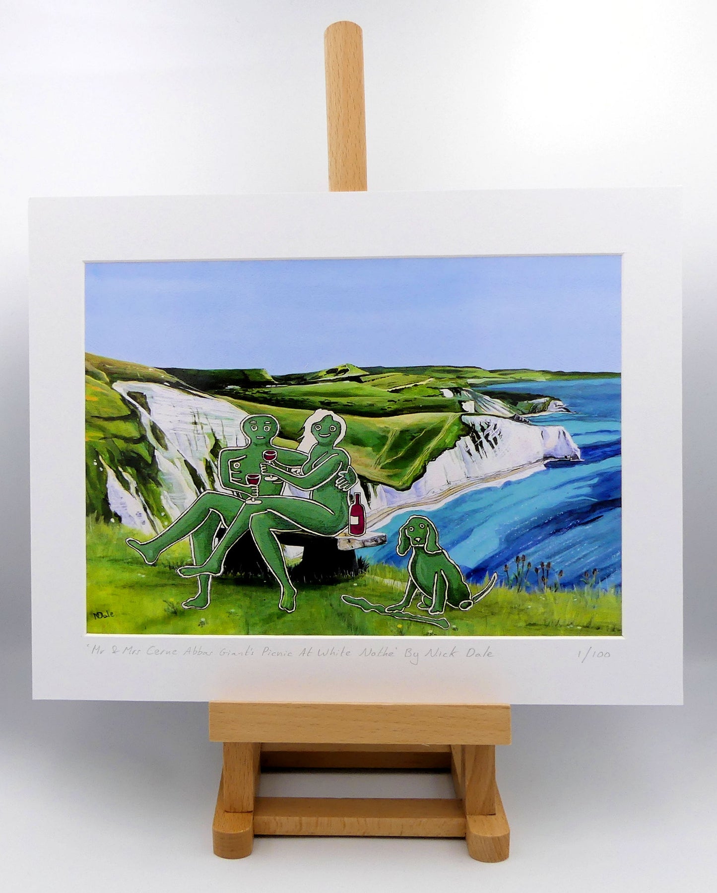 Image of a Medium Art Print featuring a copy of the composite painting 'Mr & Mrs Cerne Abbas Giant's Picnic At White Nothe' by Nick Dale. The print depicts Mr & Mrs Cerne Abbas Giant having a merlot picnic whilst on a date along the Dorset coast at the White Nothe, east of Weymouth. They are joined on the date by their cocker spaniel dog. The print is situated on a small easel.