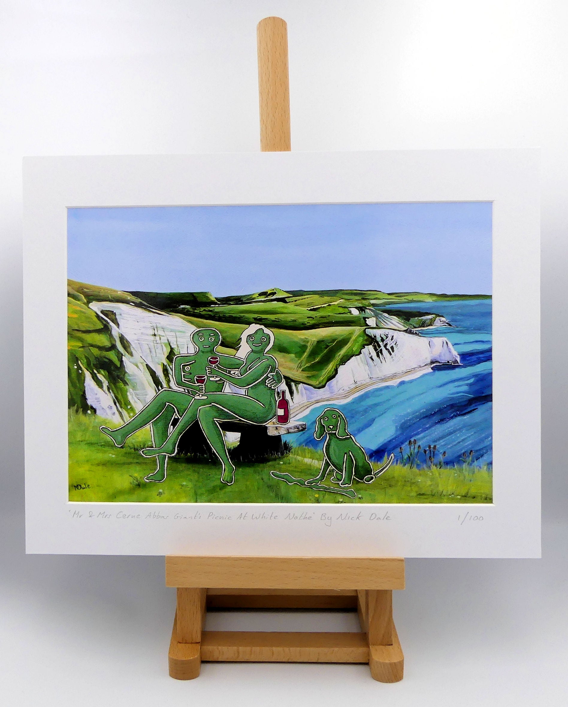 Image of a Medium Art Print featuring a copy of the composite painting 'Mr & Mrs Cerne Abbas Giant's Picnic At White Nothe' by Nick Dale. The print depicts Mr & Mrs Cerne Abbas Giant having a merlot picnic whilst on a date along the Dorset coast at the White Nothe, east of Weymouth. They are joined on the date by their cocker spaniel dog. The print is situated on a small easel.