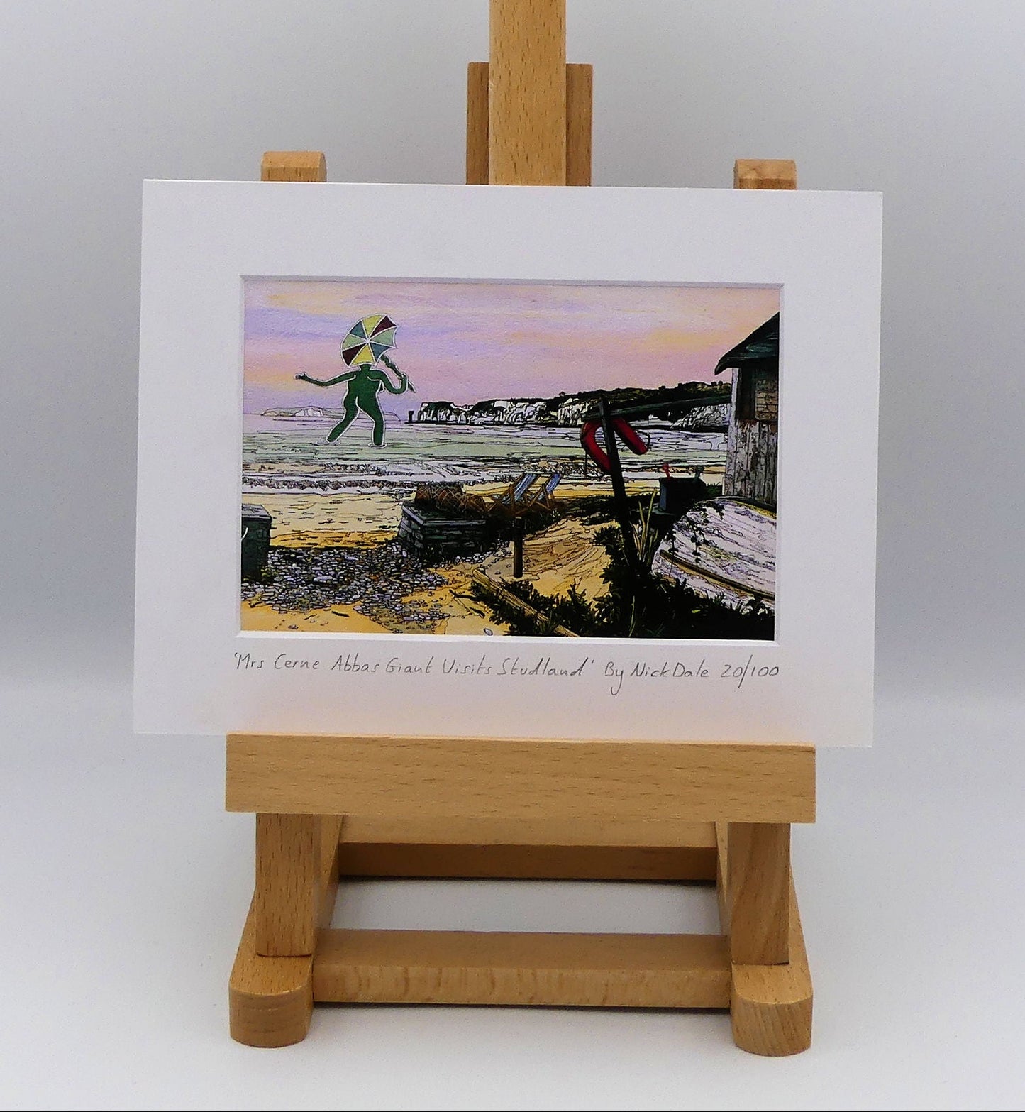 Image of a Small Art Print featuring a copy of the painting 'Mrs Cerne Abbas Giant Visits Studland' by Nick Dale. The print imagines the Cerne Abbas Giant's wife visiting the seaside at Studland Beach; with Old Harry Rocks and the Isle of Wight in the distance.  The print is situated on a small easel.