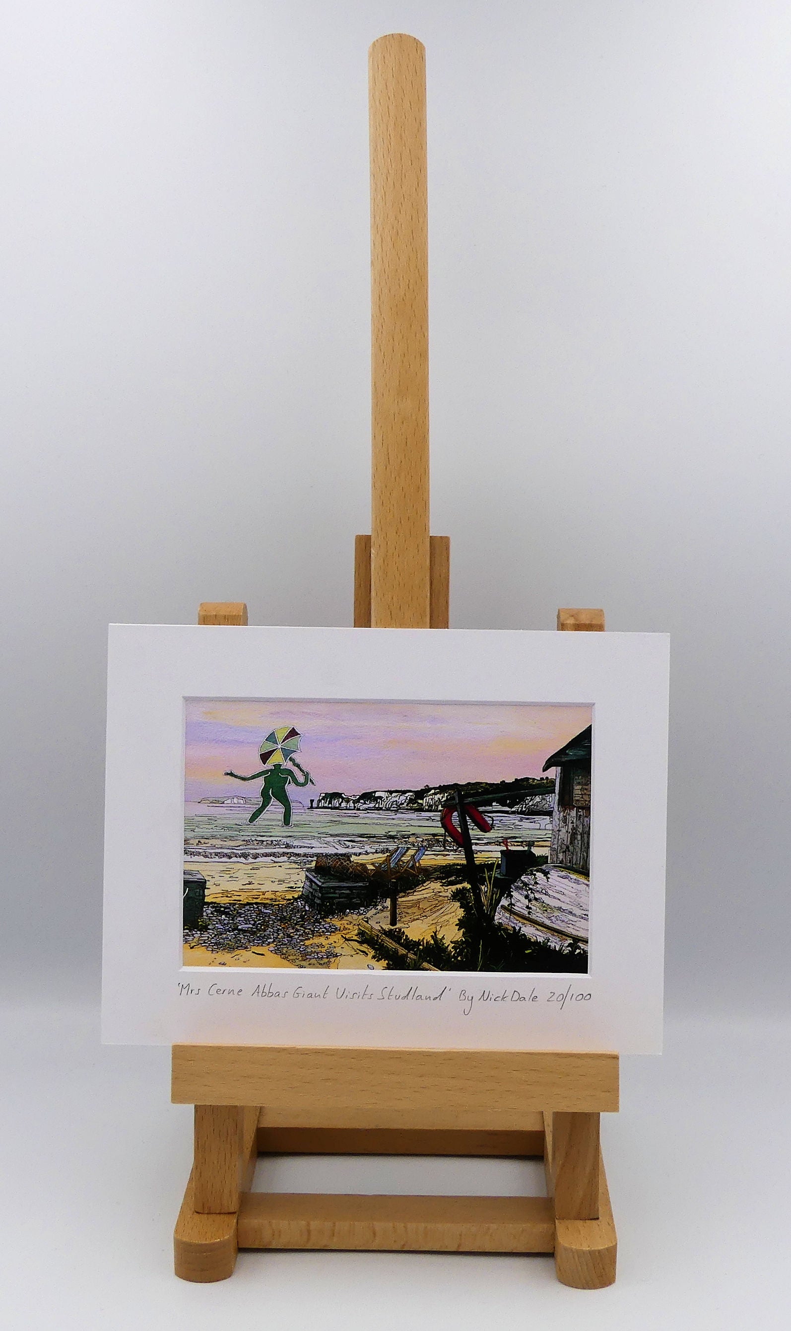 Image of a Small Art Print featuring a copy of the painting 'Mrs Cerne Abbas Giant Visits Studland' by Nick Dale. The print imagines the Cerne Abbas Giant's wife visiting the seaside at Studland Beach; with Old Harry Rocks and the Isle of Wight in the distance. The print is situated on a small easel.