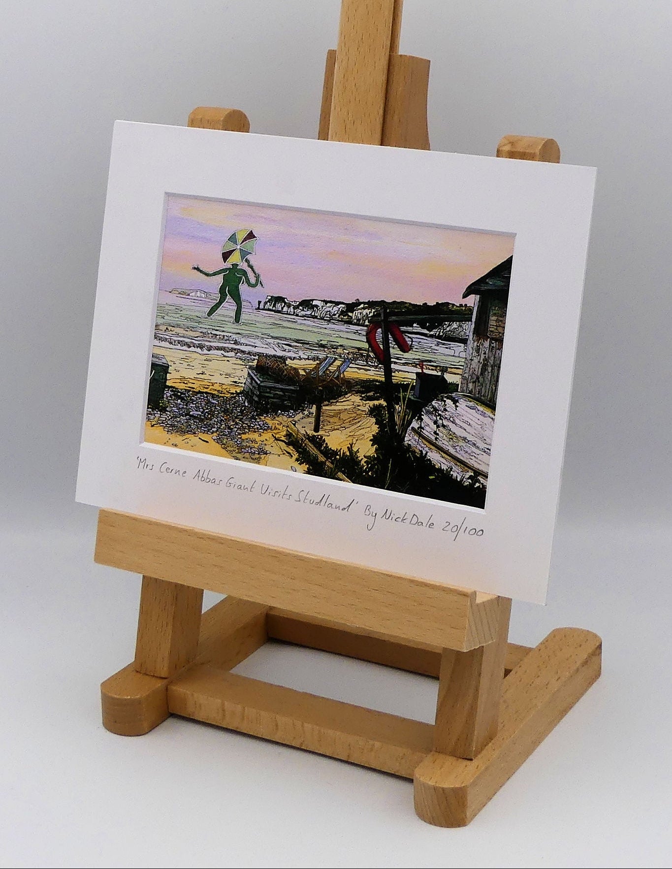 Image of a Small Art Print featuring a copy of the painting 'Mrs Cerne Abbas Giant Visits Studland' by Nick Dale. The print imagines the Cerne Abbas Giant's wife visiting the seaside at Studland Beach; with Old Harry Rocks and the Isle of Wight in the distance. The print is situated on a small easel.