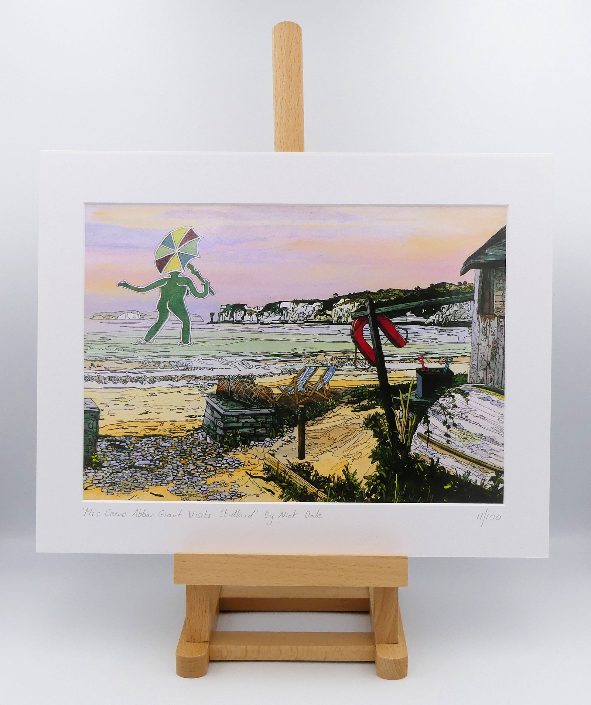 Image of a Medium Art Print featuring a copy of the painting 'Mrs Cerne Abbas Giant Visits Studland' by Nick Dale. The print imagines the Cerne Abbas Giant's wife visiting the seaside at Studland Beach; with Old Harry Rocks and the Isle of Wight in the distance. The print is situated on a small easel.