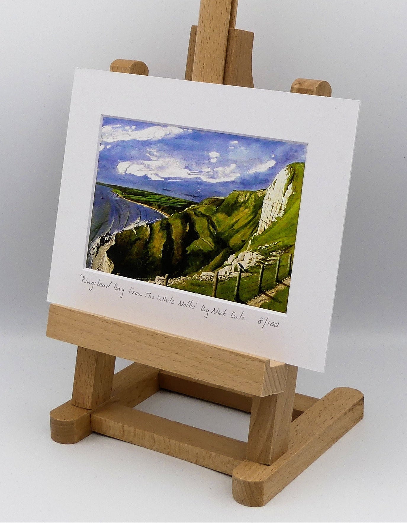 Image of a Small Art Print featuring a copy of the painting 'Ringstead Bay From The White Nothe' by Nick Dale. The print depicts a view along the Jurassic Coast from the White Nothe chalk headland east of Ringstead Bay. The view looks west over the bay to the village of Ringstead & beyond. The print is situated on a small easel.